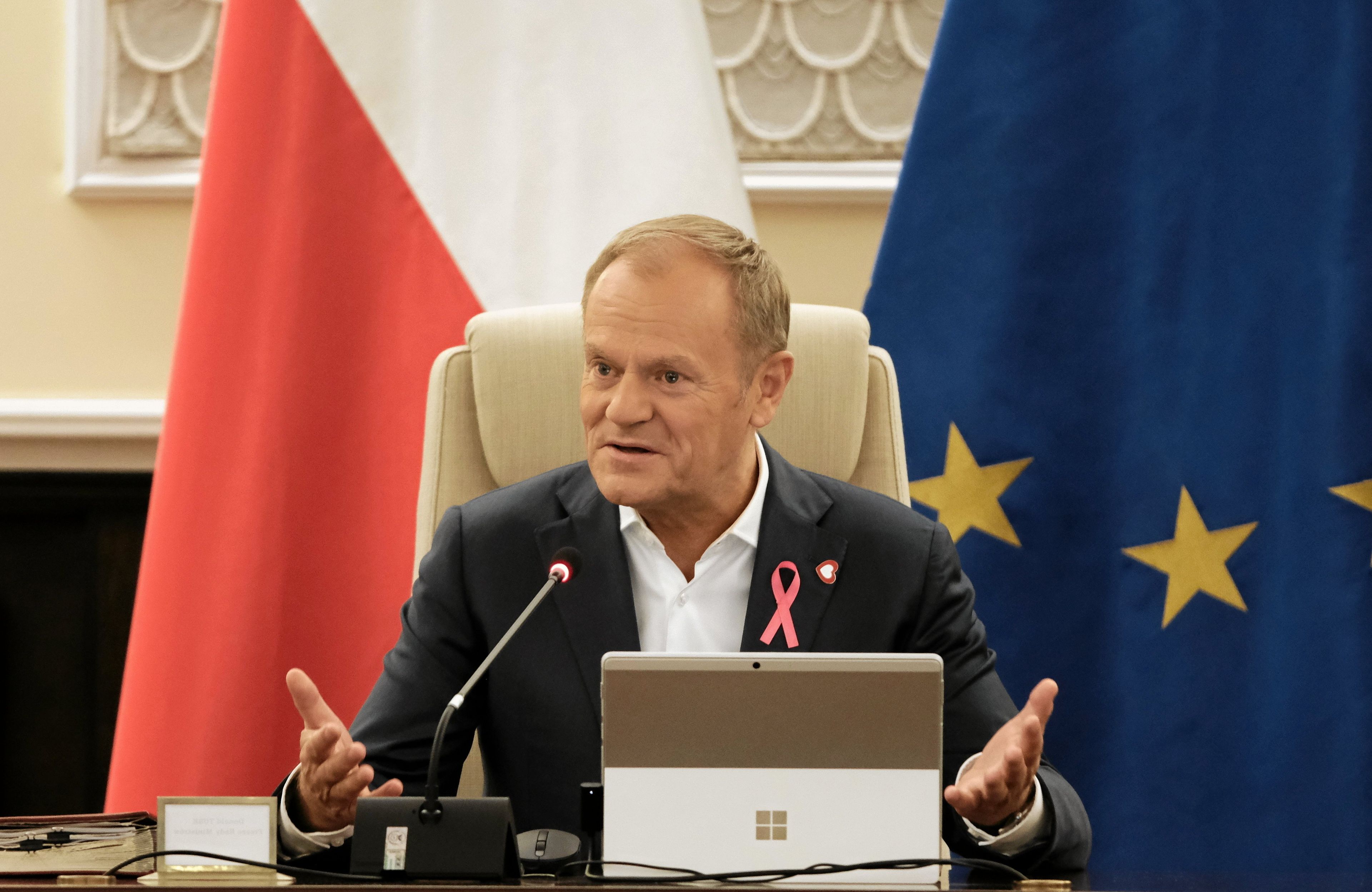 Donald Tusk za stołem podczas posiedzenia rządu, za nim flagi Polski i UE