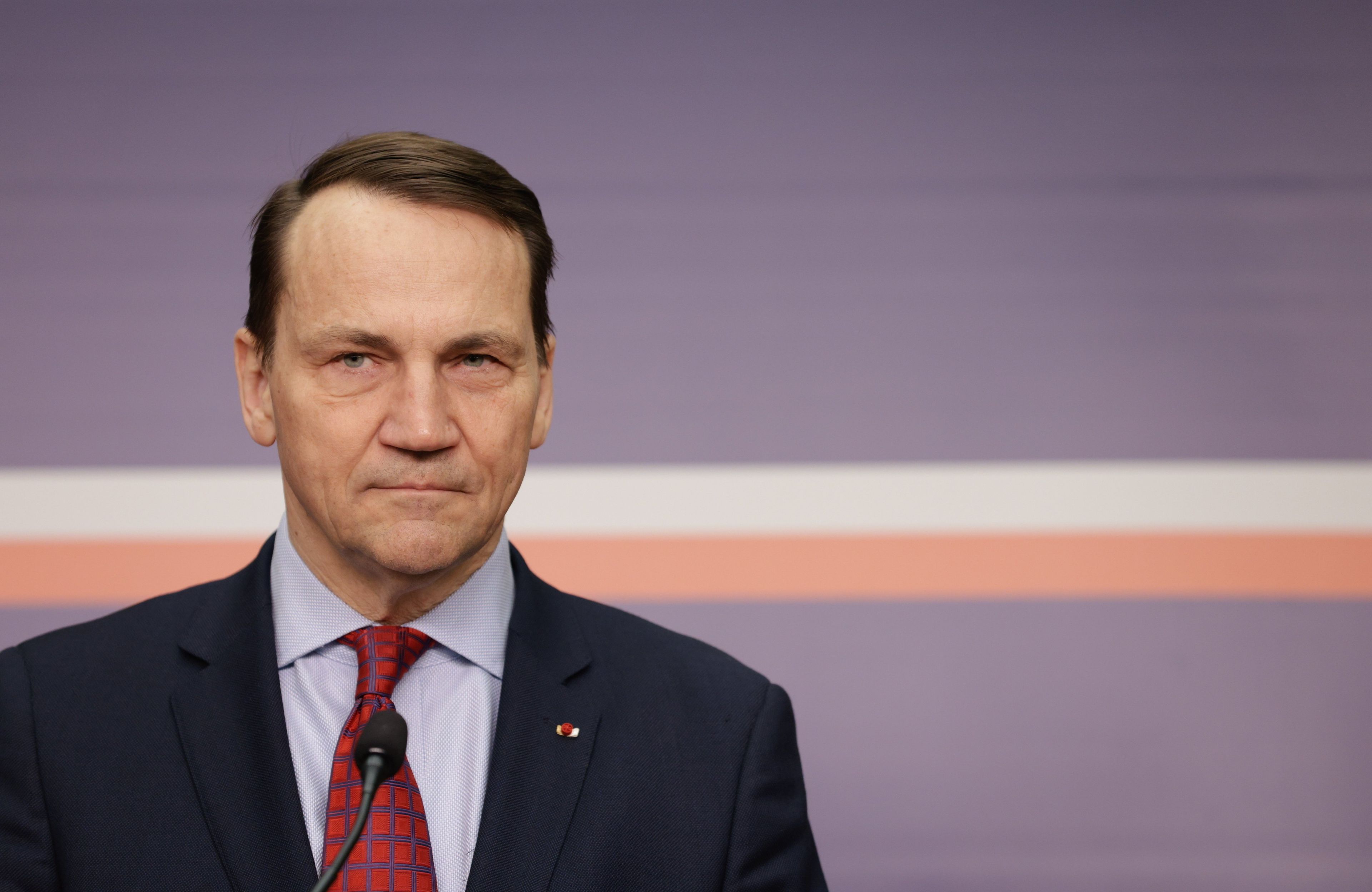 Szef polskiej dyplomacji Radosław Sikorski na tle ciemnoniebieskiej ściany z biało-czerwonym paskiem