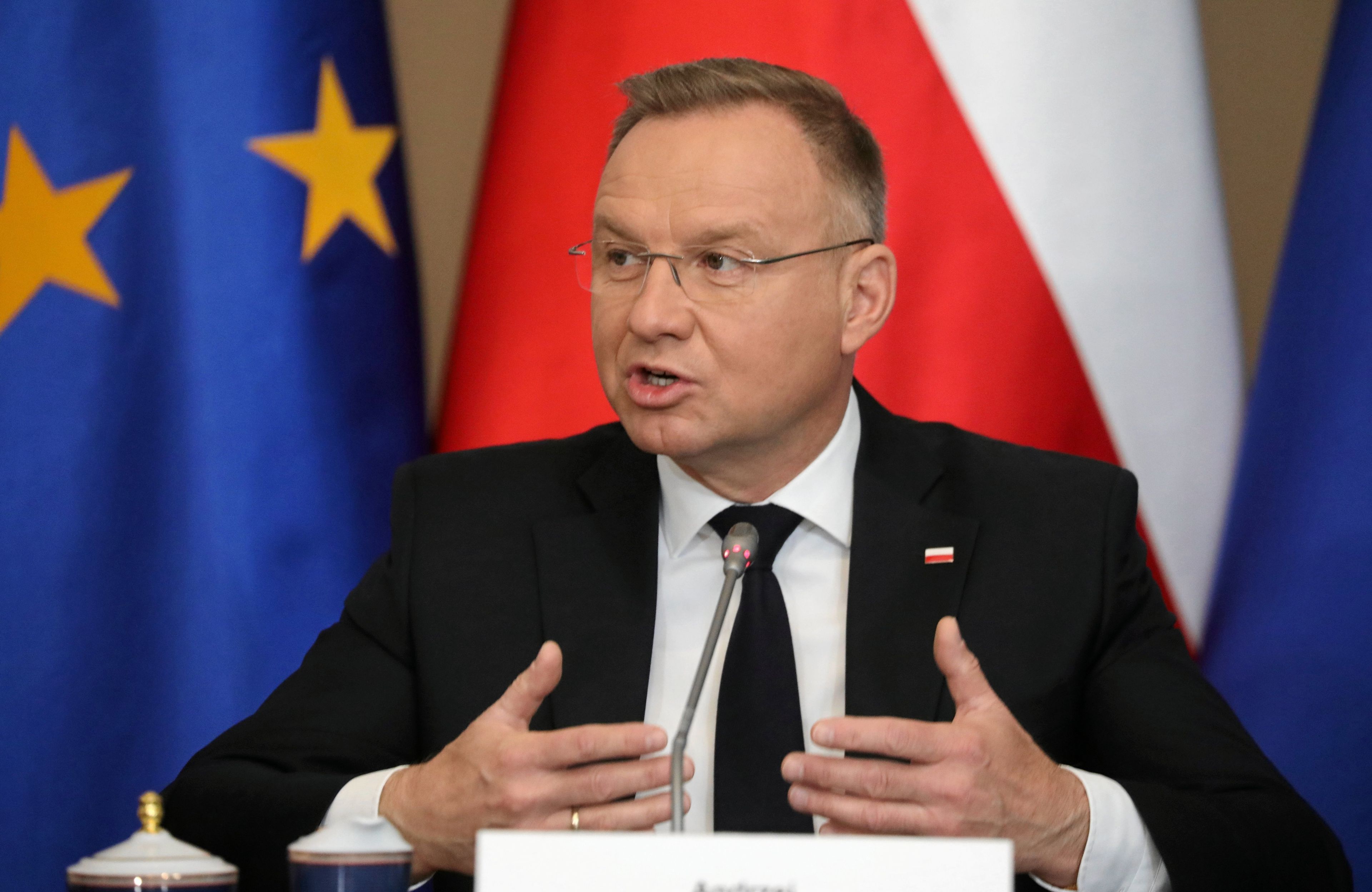 Duda siedzi na tle flag i mówi