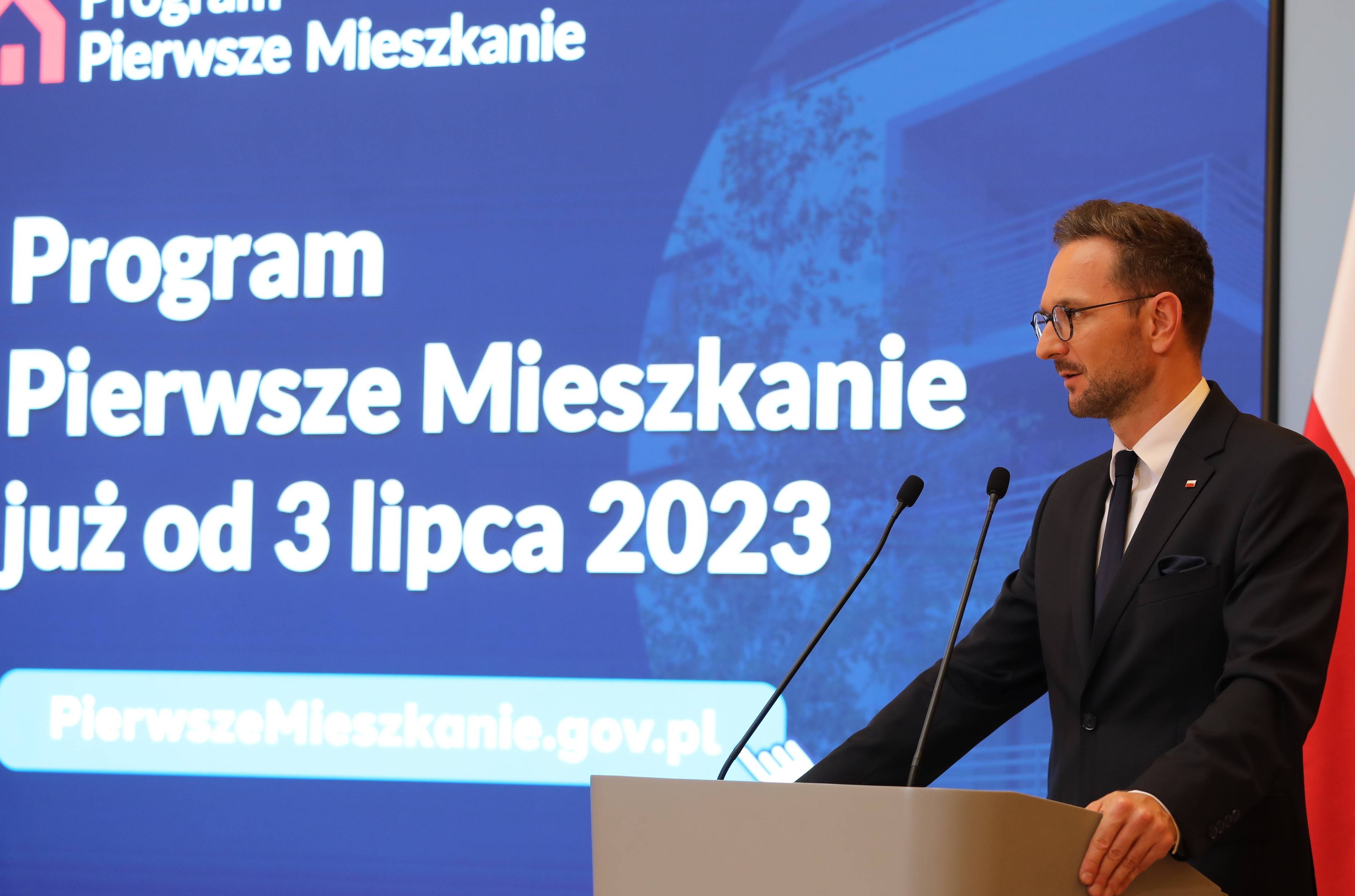 Mężczyzna przy mównicy (Waldemar Buda) na tle napisu "Program Pierwsze Mieszkanie już od 3 lipca 2023"