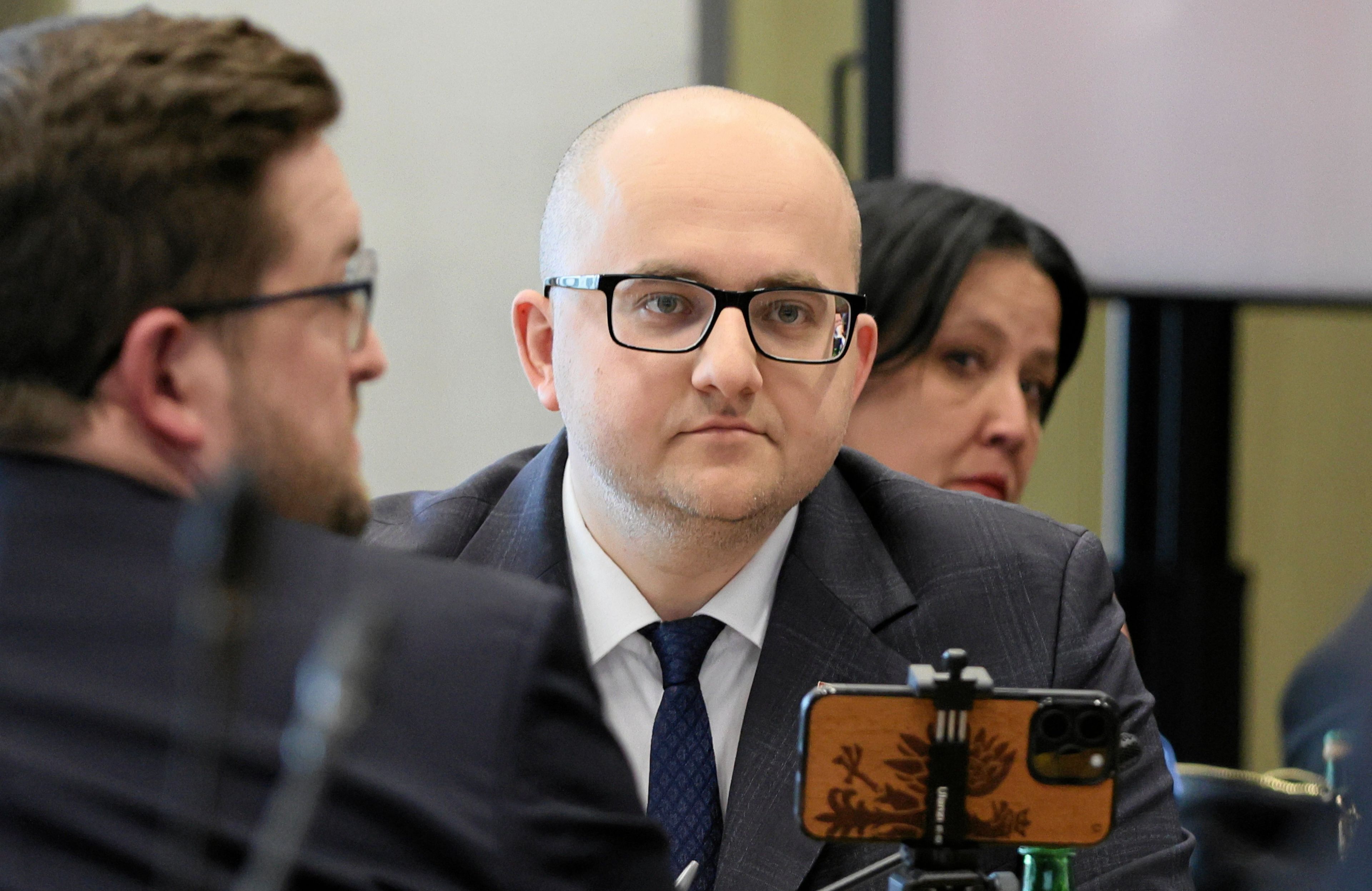 Łysy mężczyzna w okularach (poseł PiS Dariusz Matecki), siedzi przed ustawionym na statywie smartfonie