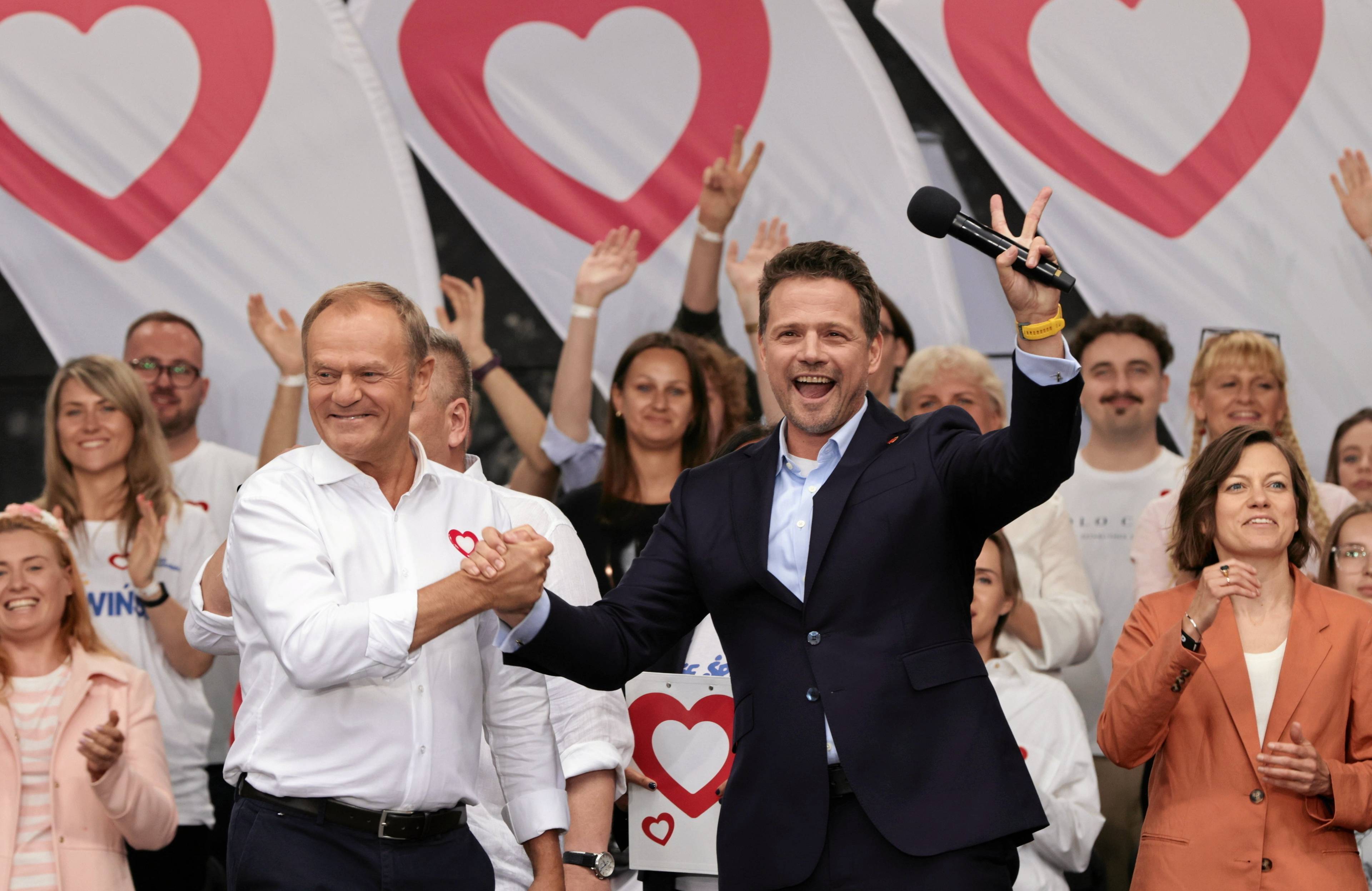 Donald Tusk i Rafał Trzaskowski podają sobie ręce w geście radości, Trzaskowski pokazuje przy tym gest zwycięstwa