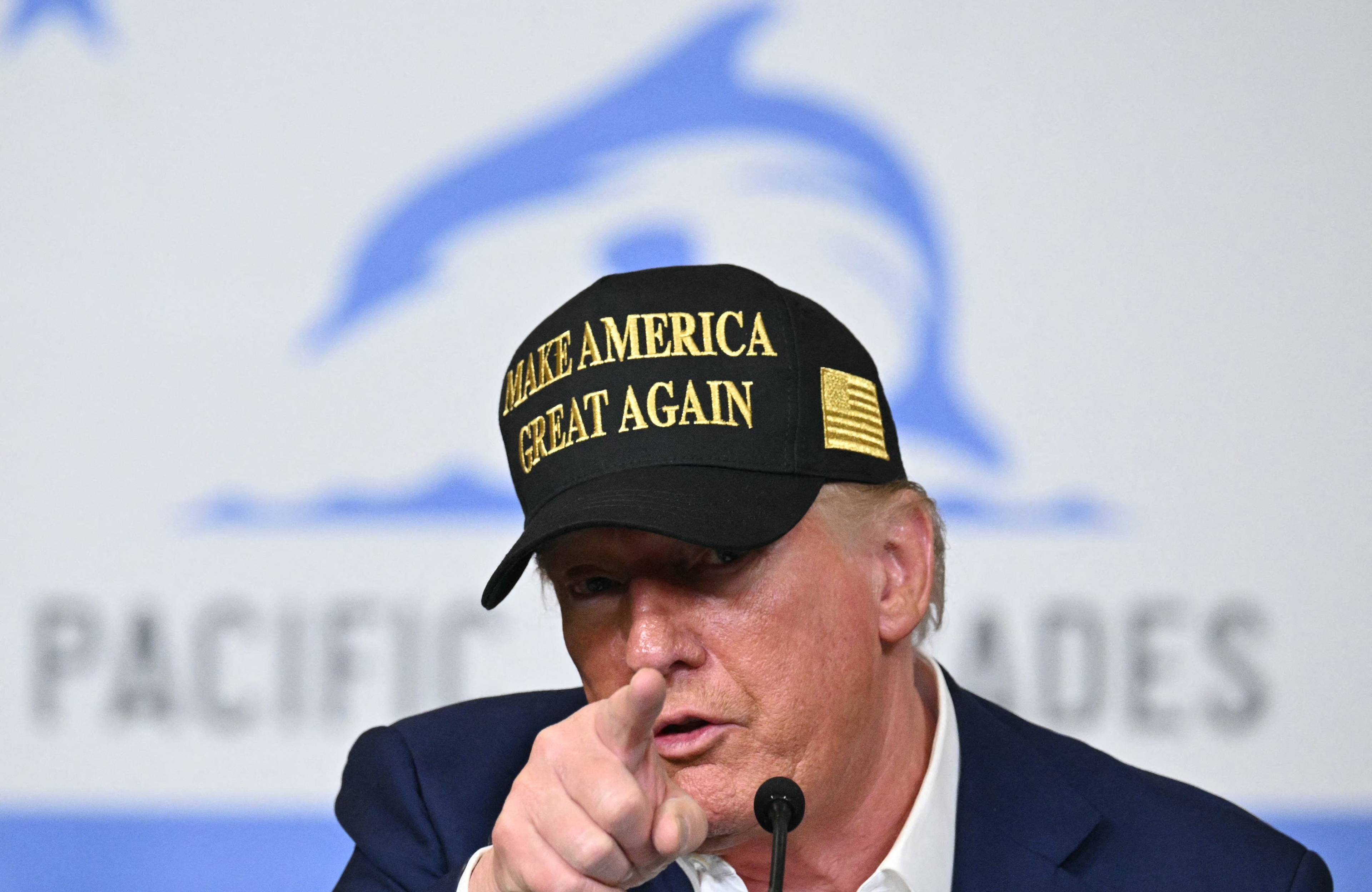 Mężczyzna w czapce z napisem Make America Great Again wskazuje palcem w obiekty kamery