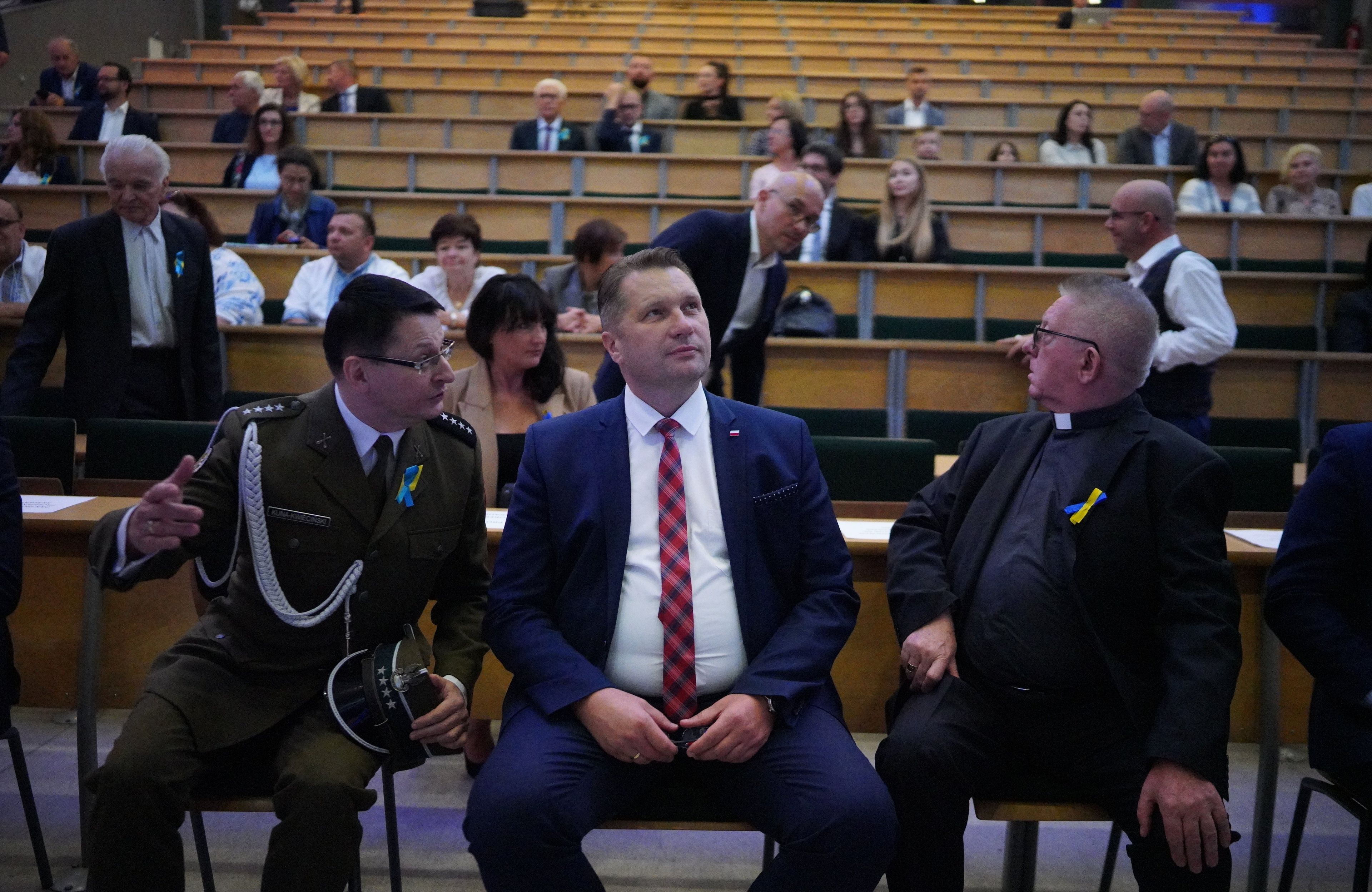 Minister Czarnek siedzi w auli pomiędzy księdzem i wojskowym