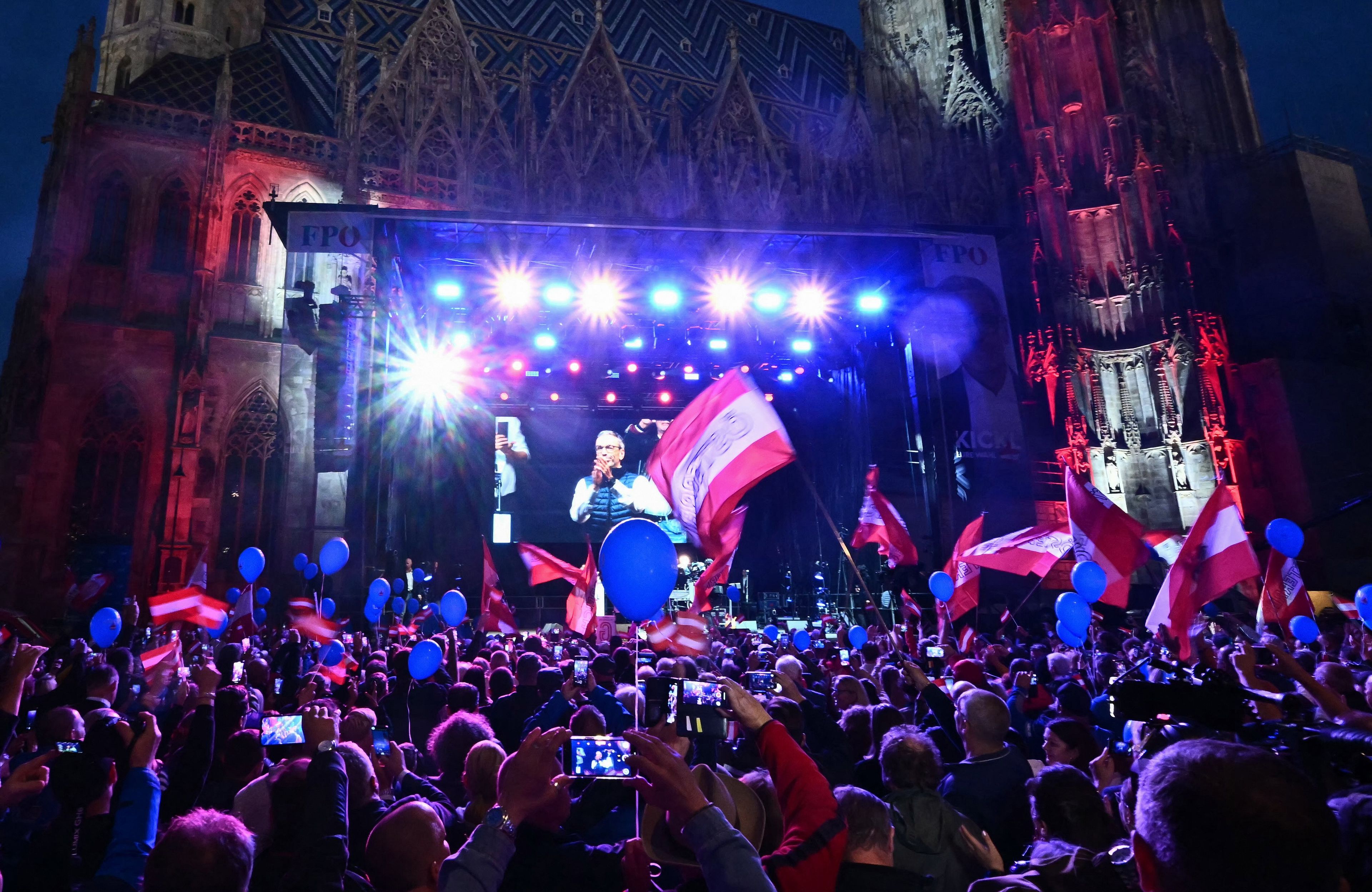 Wiec wyborczy, ludzie słuchają polityków przemawiających na tle austriackich flag