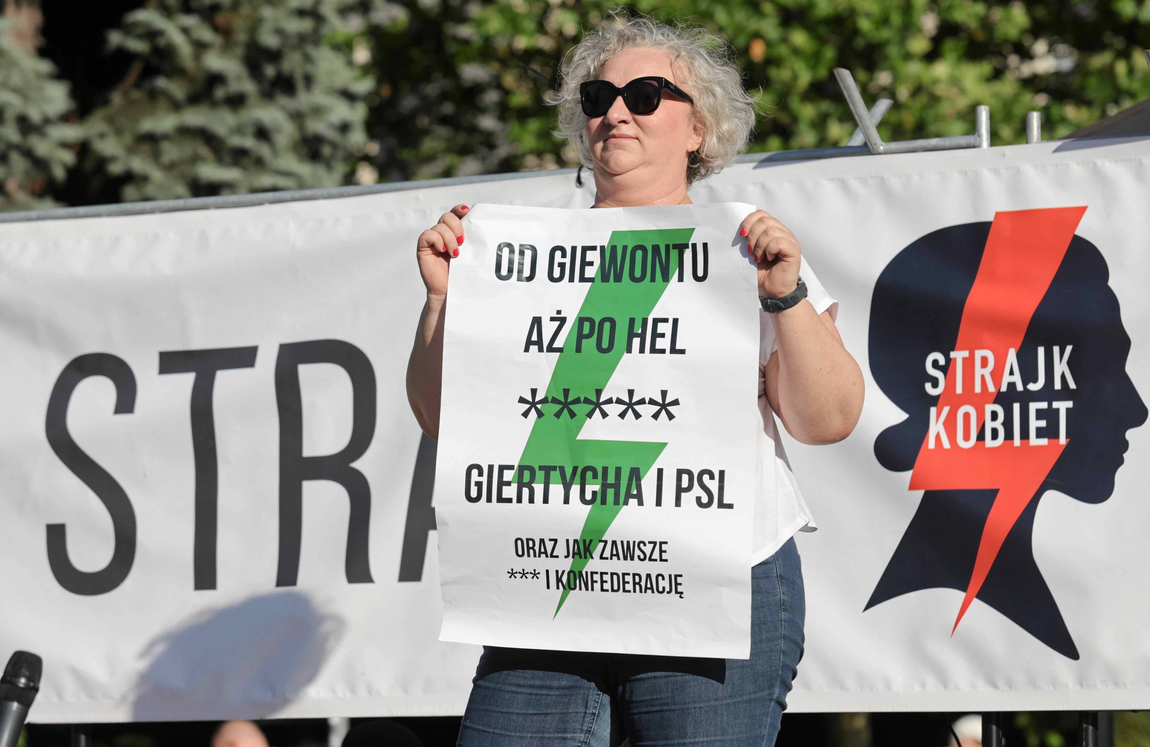 Kobieta stoi na scenie podczas demonstracji trzymając plakat z napisem Od Giewontu aż po Hel [pięć gwiazdek] Giertycha i PSL