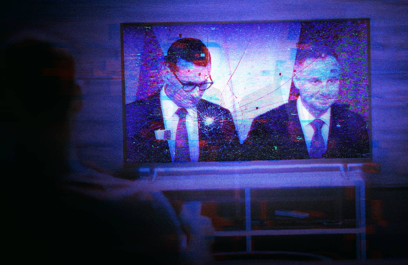 Ciemne mieszkanie, rozświetlony, pęknięty ekran telewizora, na którym wyświetlony jest Mateusz Morawiecki i Andrzej Duda