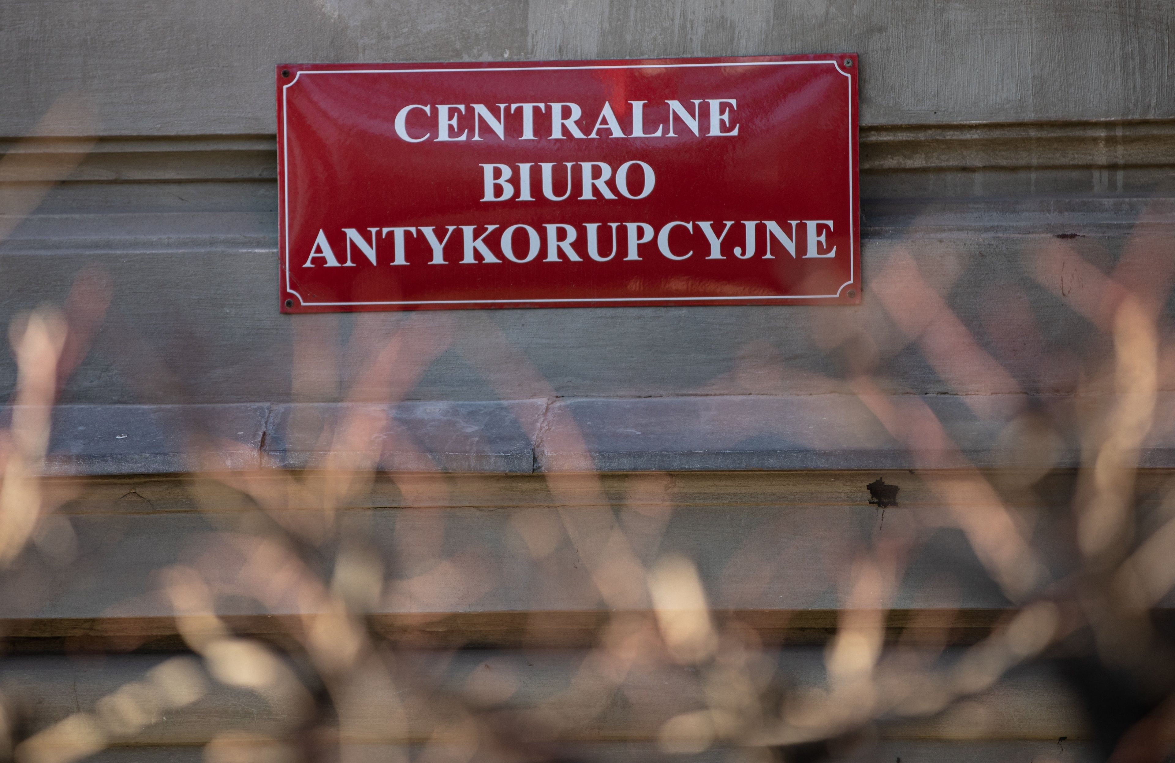 Napis na czerwonej tabliczce: Centralne Biuro Antykorupcyjne i jakieś krzaki