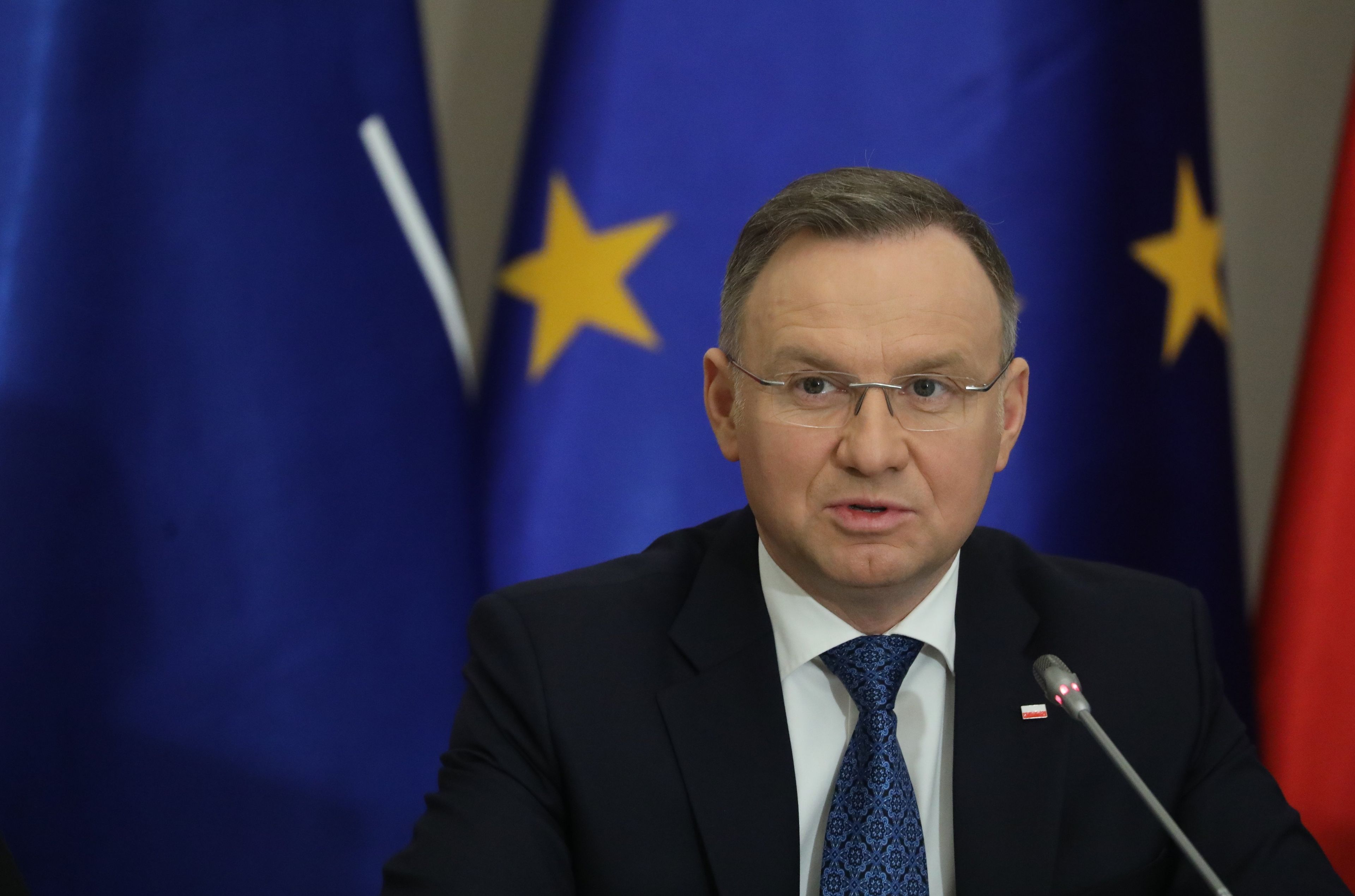 Mężczyzna siedzi, w okularach, na tle flag