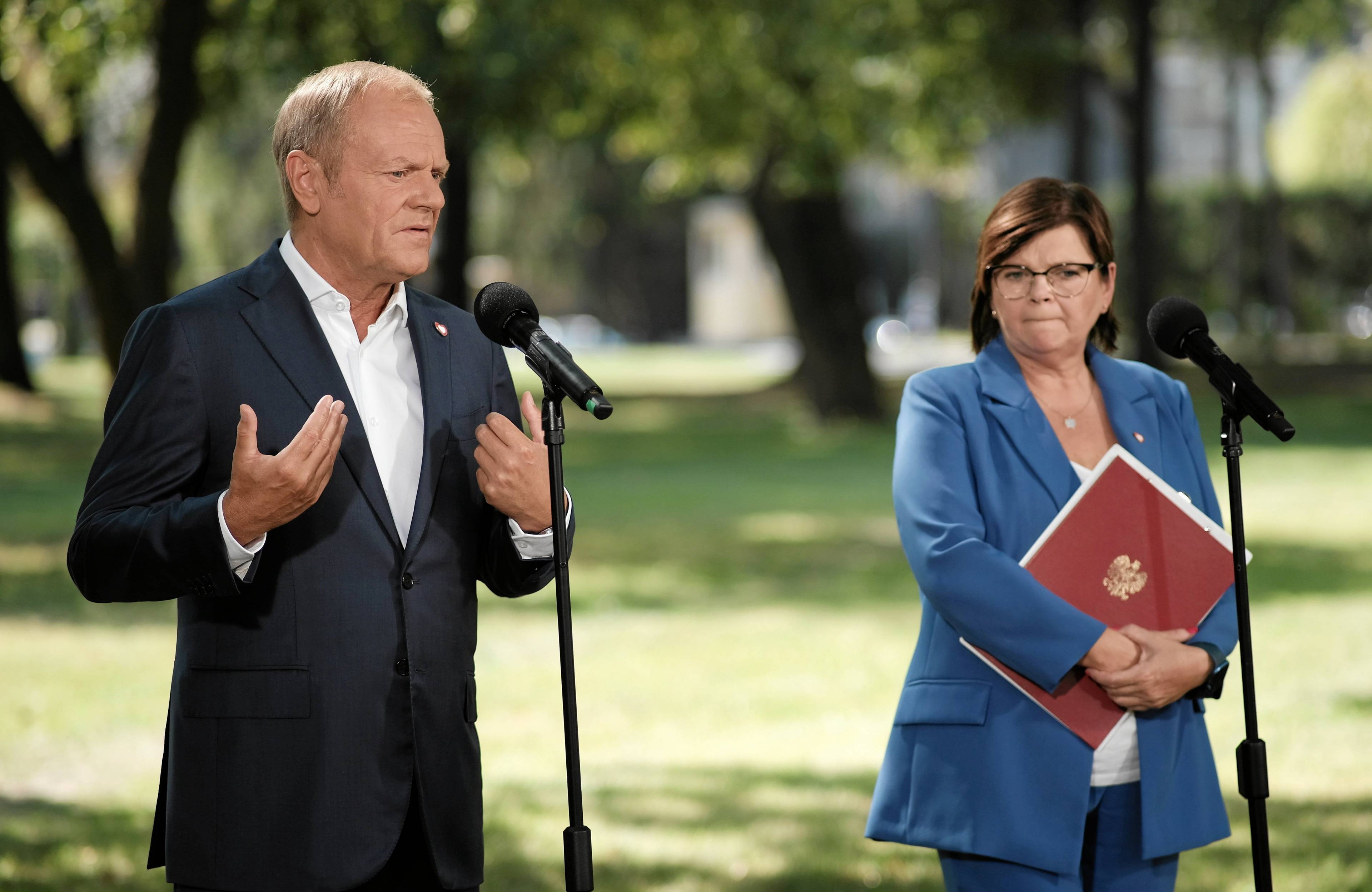 Donald Tusk i Izabela Leszczyna podczas konferencji. W tle trawnik i drzewa