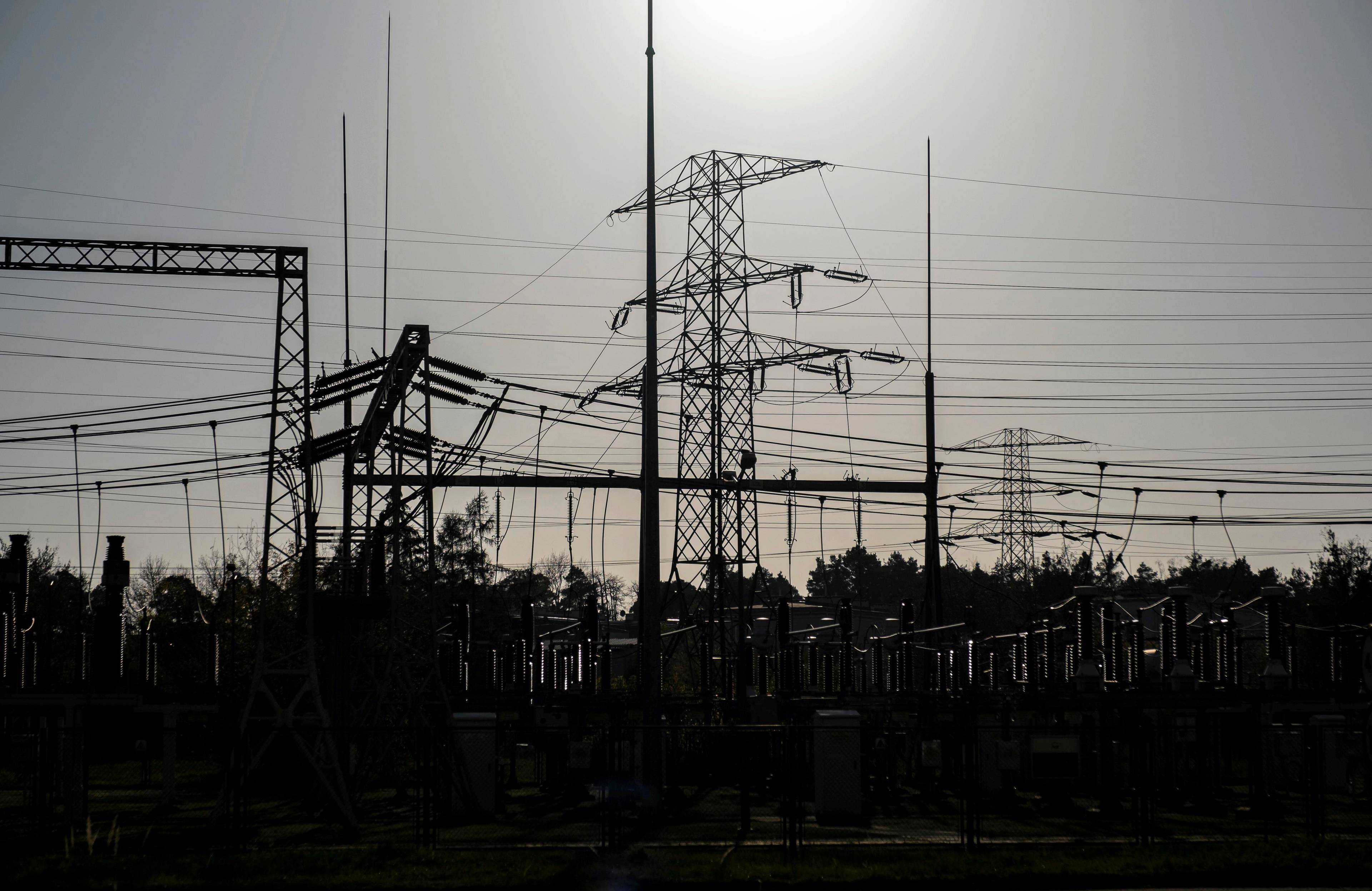 Słup energetyczny i liny wysokiego napięcia na tle słabego słońca