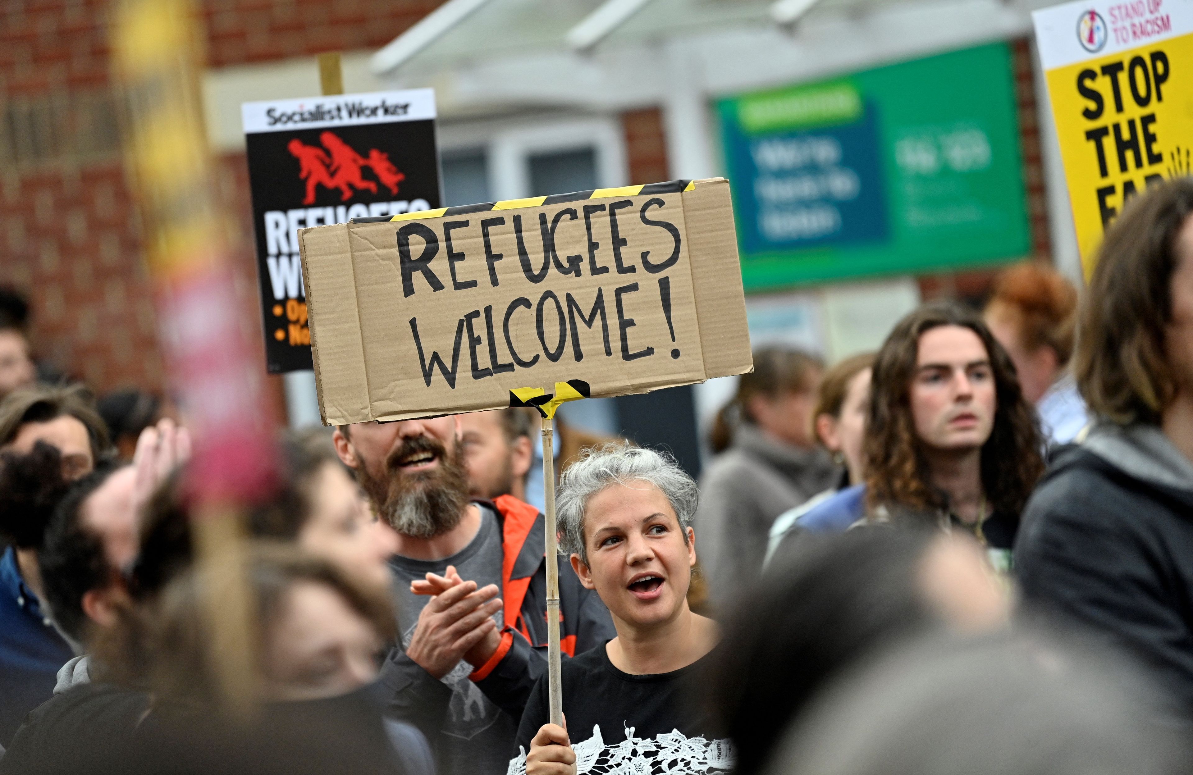 osoba stojąca w tłumie z transparentem refugees welcome