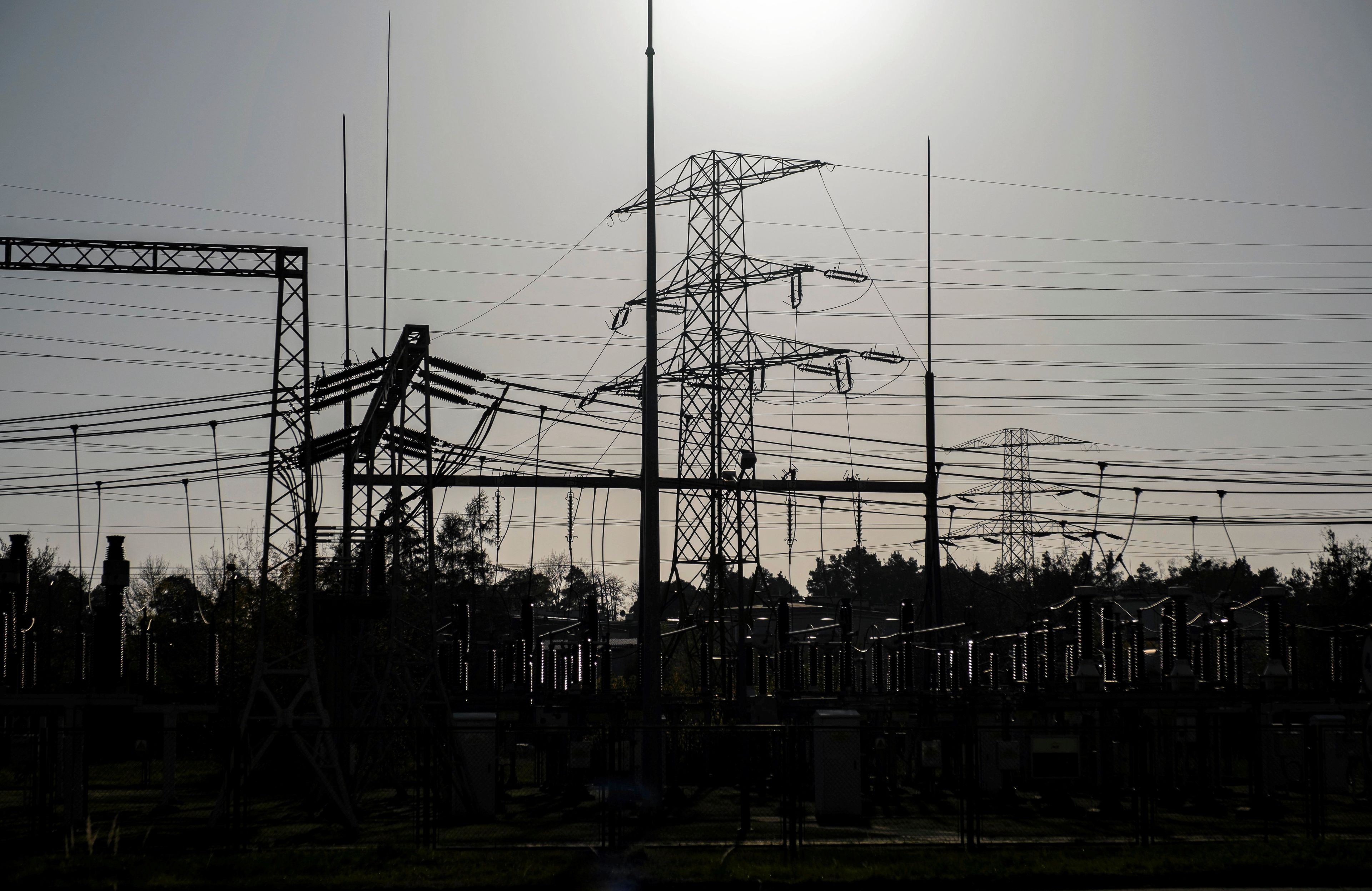 Słup energetyczny i liny wysokiego napięcia na tle słabego słońca