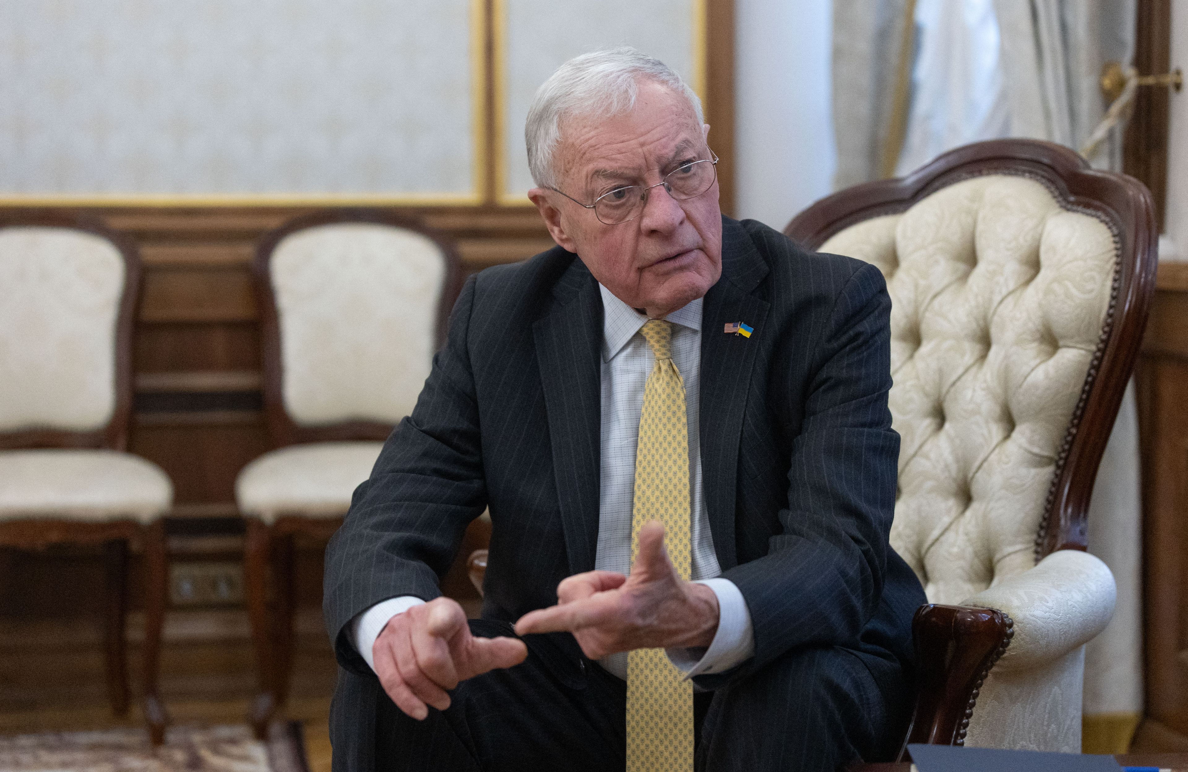 Mężczyzna w garniturze, z żółtym krawatem siedzi na pikowanym fotelu i coś wylicza na palcach. Keith Kellogg