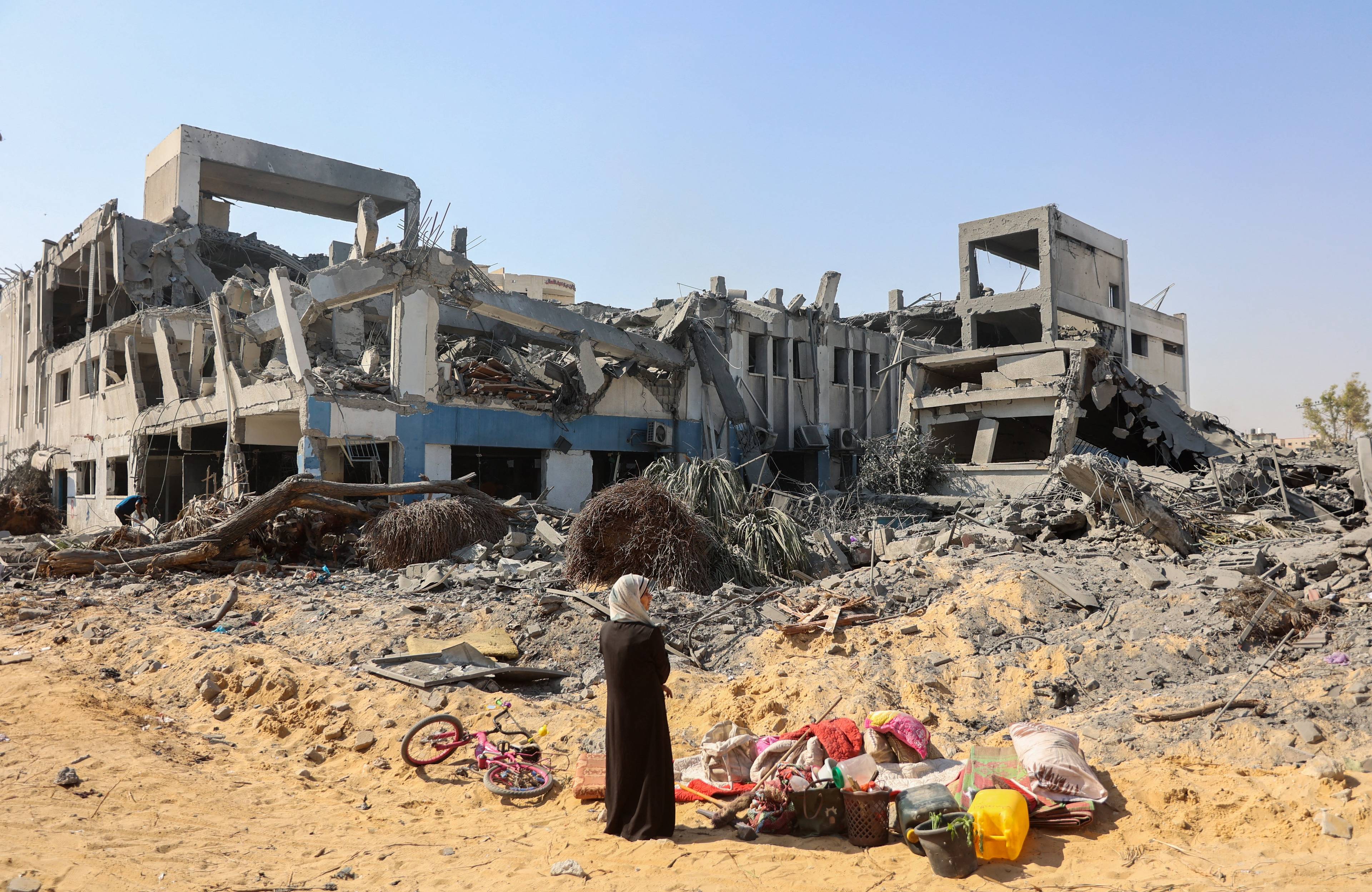 Kobieta stoi przez zniszczonym budynkiem w Gazie, na ziemi leżą pakunki