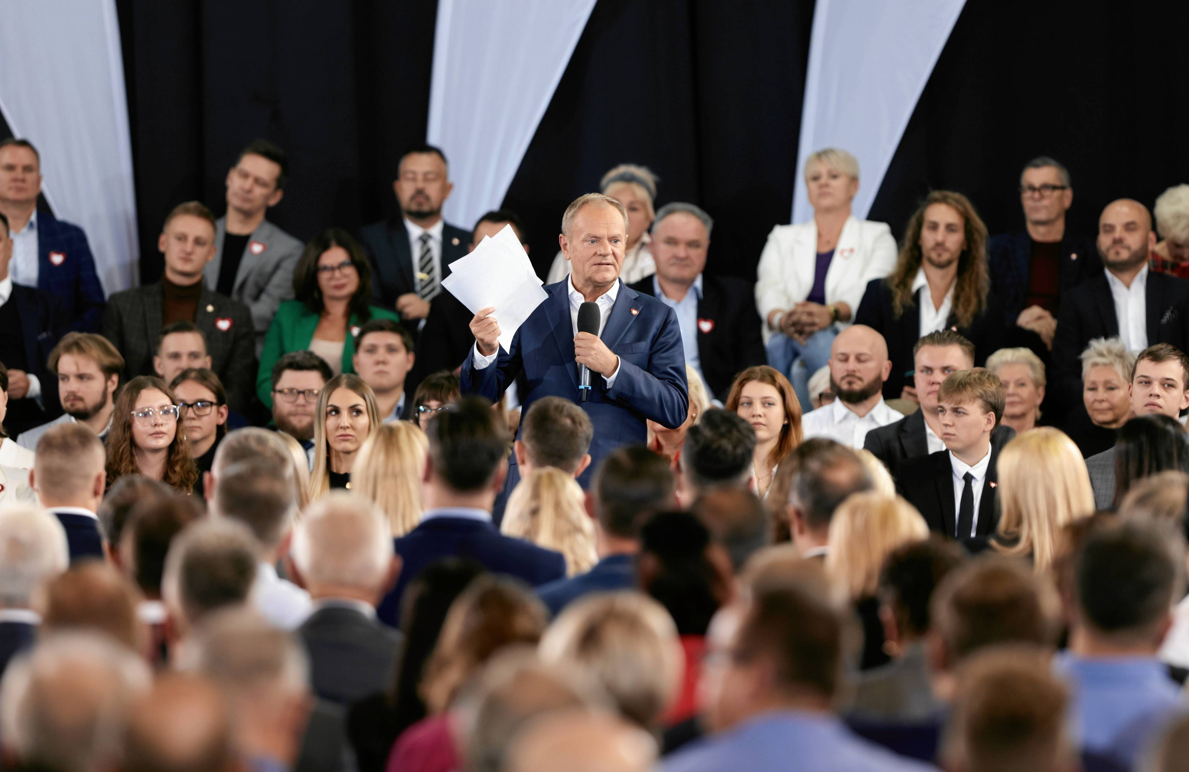 Donald Tusk otoczony uczestnikami partyjnej konwencji pokazuje plik papierów