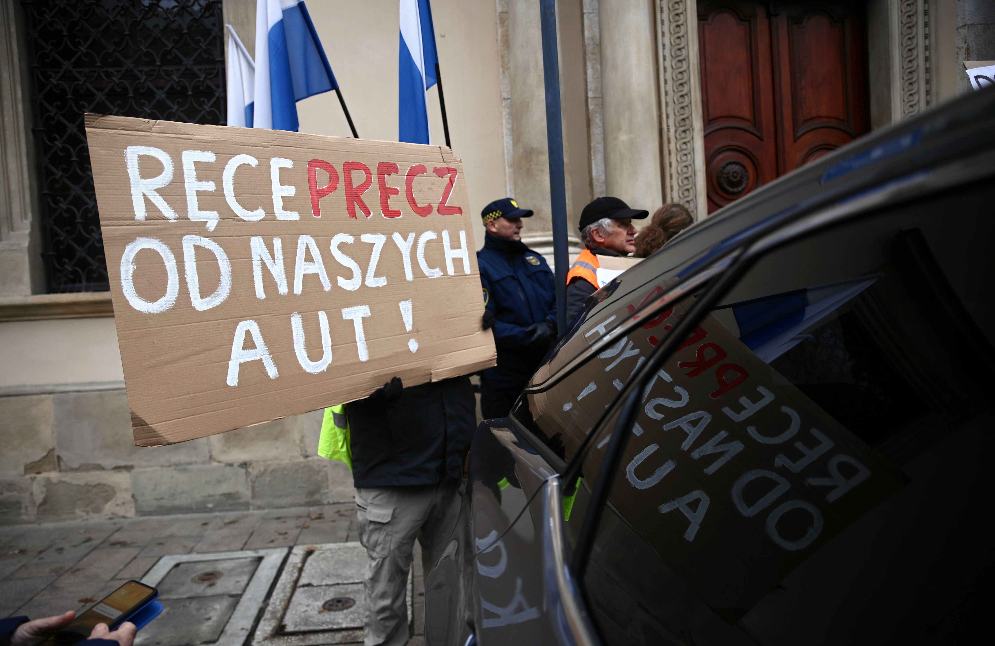 baner "ręce precz od naszych aut" wystawiony przez kierowcę z wnętrza samochodu przed zabytkowym budynkiem