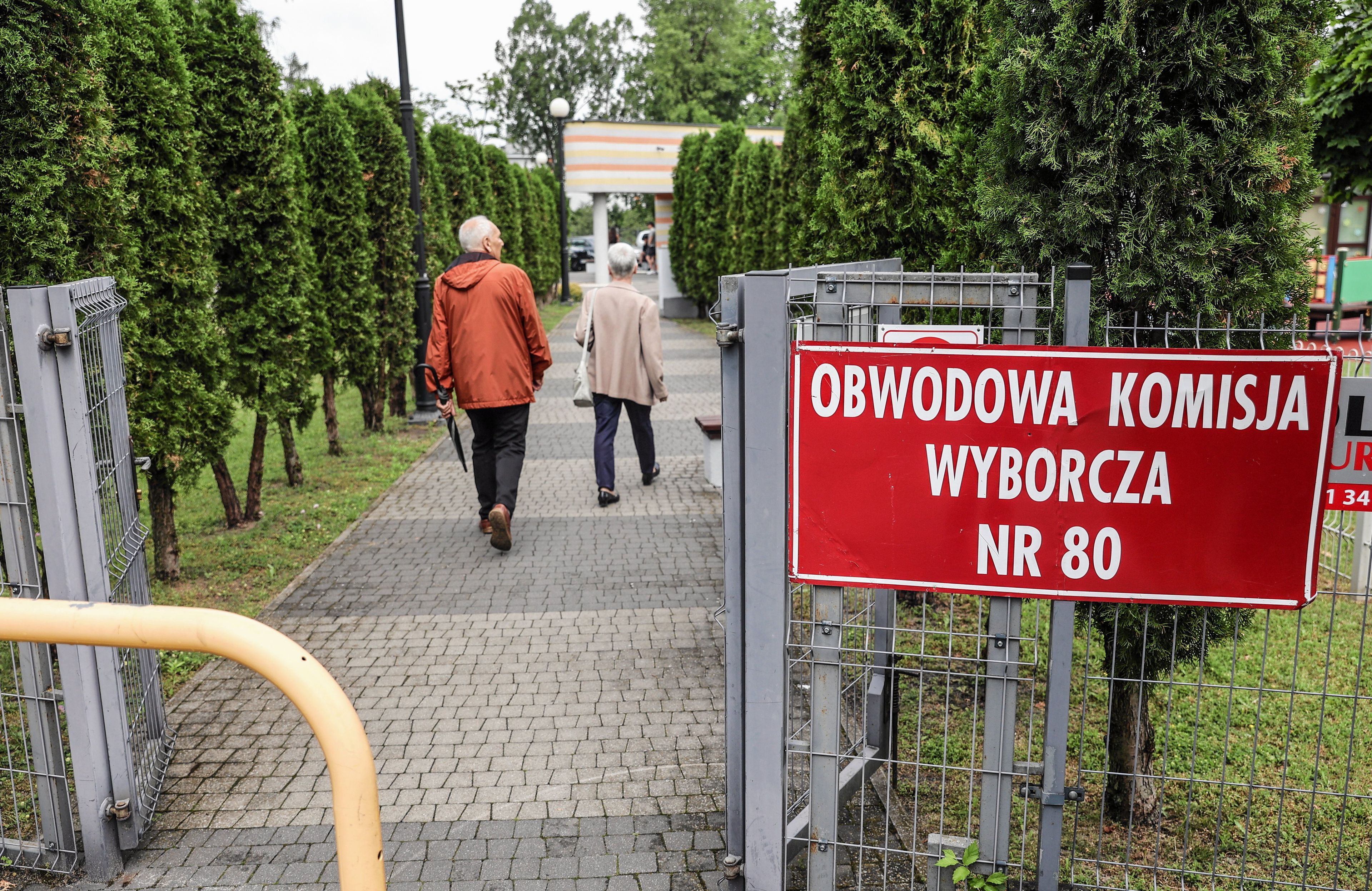 Osoby idą do komisji wyborczej, z prawej strony tabliczka z nazwą komisji