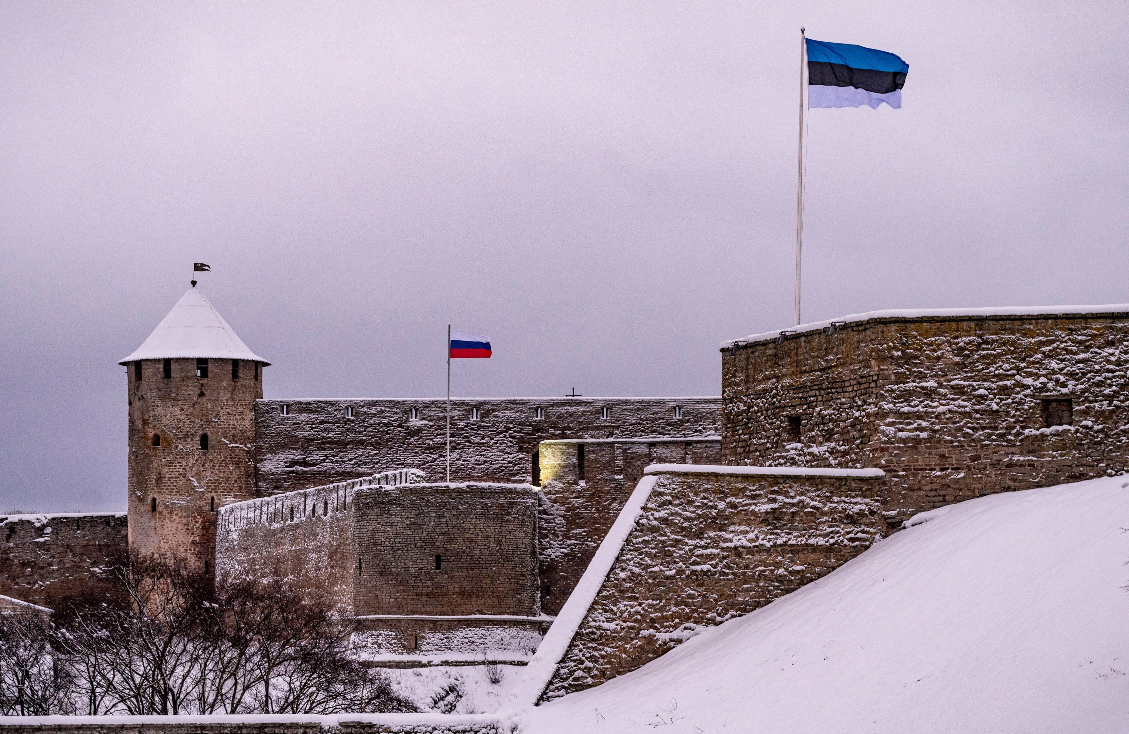Ośnieżony zamek w Narwie na granicy rosyjsko-estońskiej, w dali powiewa flaga rosyjska, bliżej widać estońską