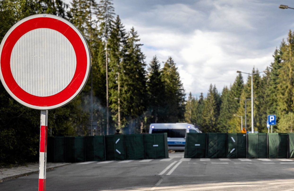 Zamknięta granica. Na pierwszym planie znak zakazu ruchu, na dugim zapora i policyjna furgonetka.