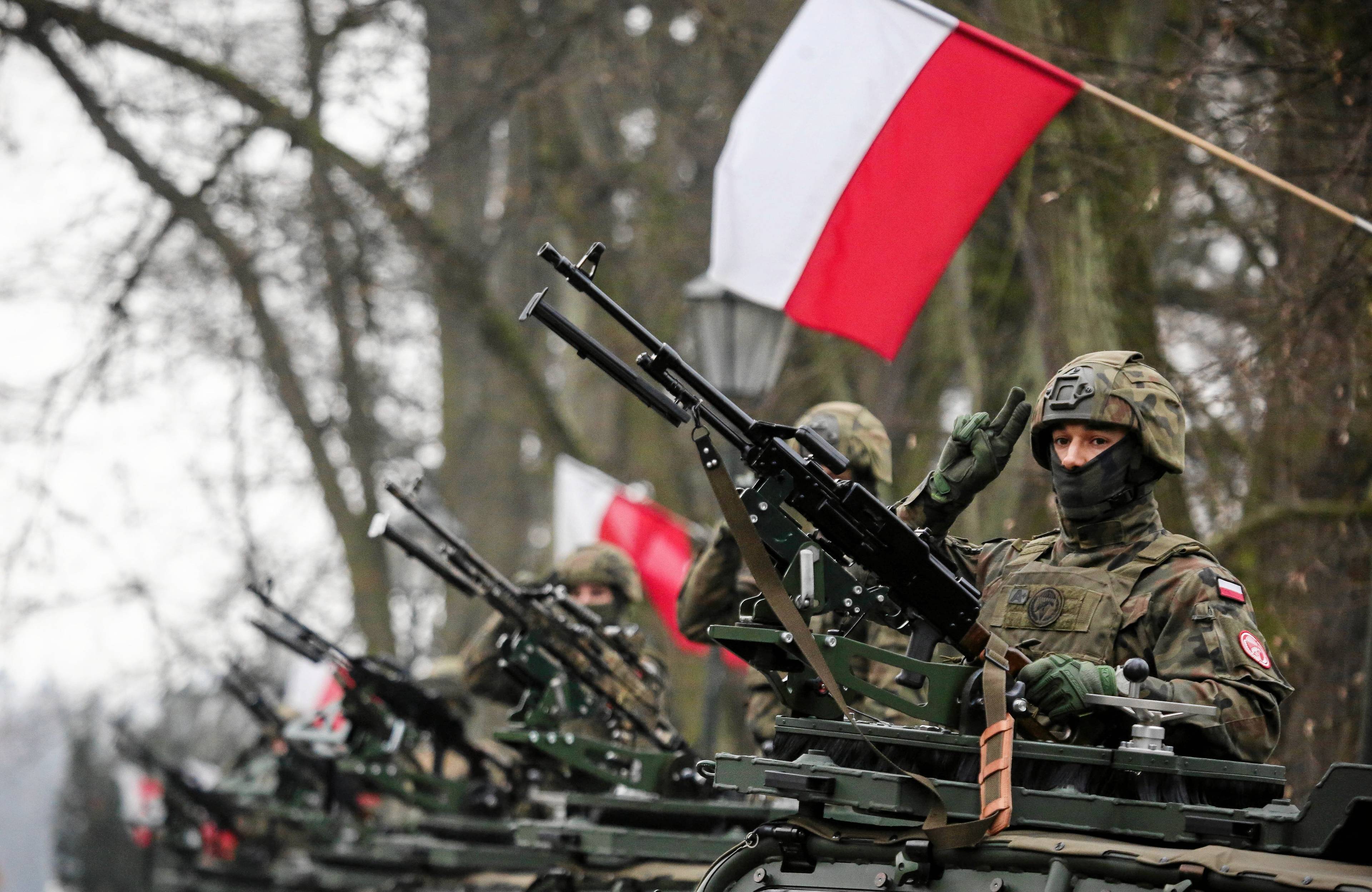 żołnierze z bronią w rzędzie pod polskimi flagami
