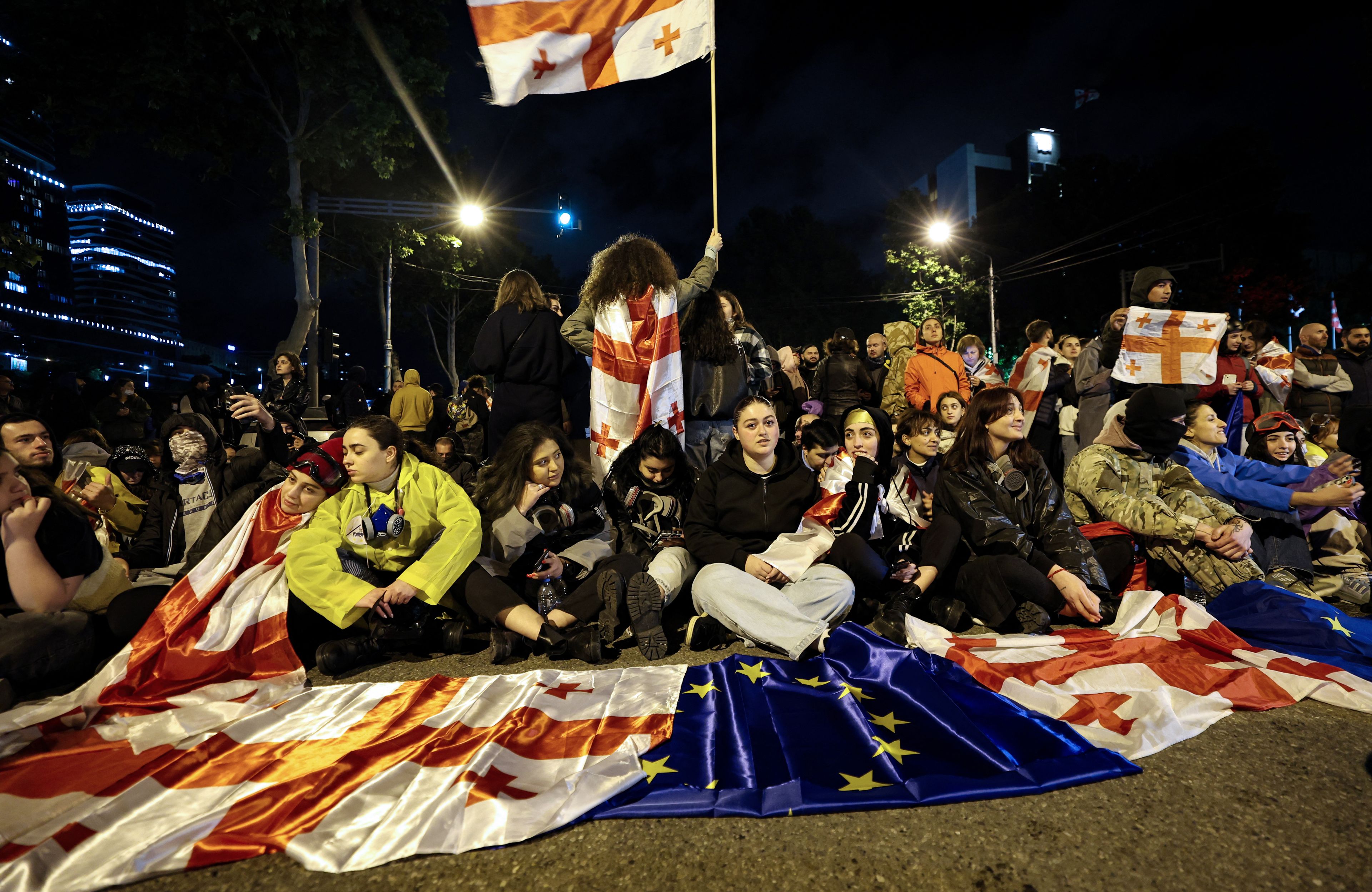 Młodzi ludzie siedza na jezdni z flagami Gruzji i UE