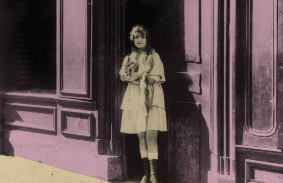 Młoda dziewczyna stoi na ulicy przed wejściem do kamienicy.