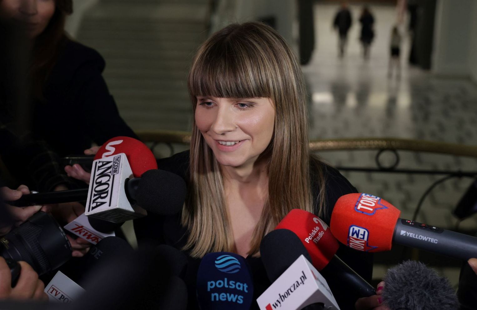 Młoda usmiechnieta kobieta otoczona reporterami