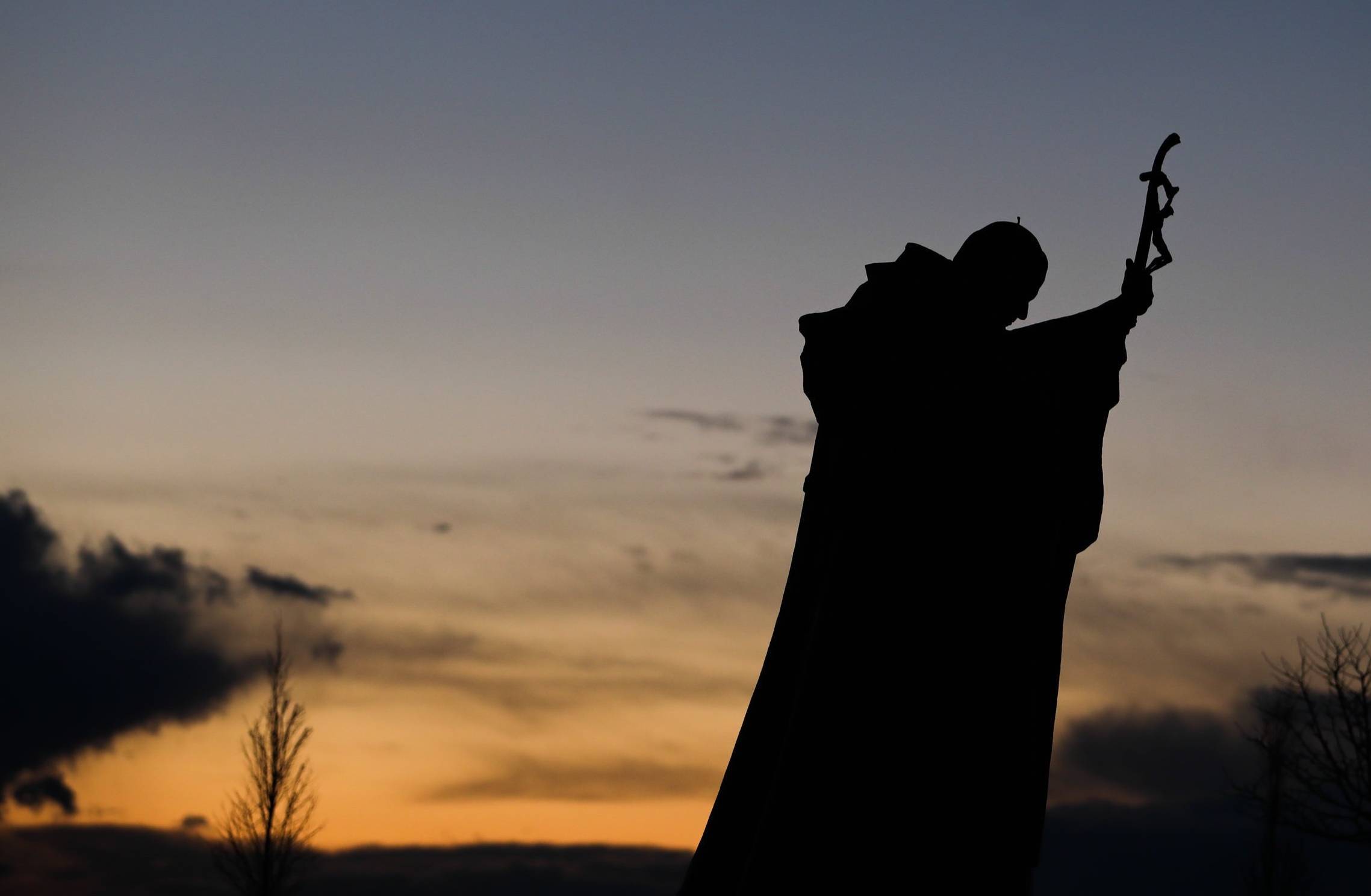 Pomnik papieża Jana Pawła II na tle nieba o zmierzchu.