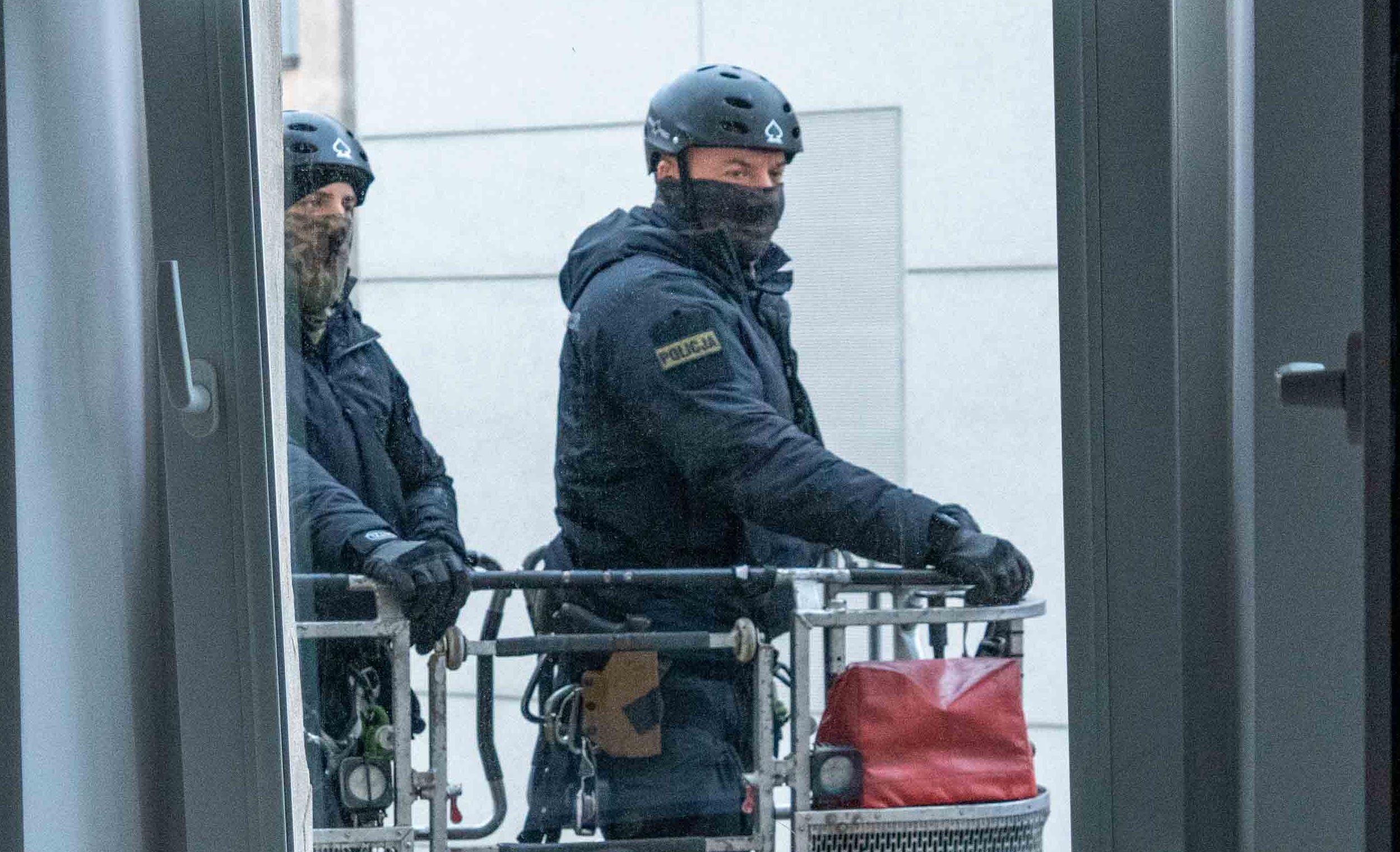 Dwóch policjantów widać przez okno, stoją na podnośniku