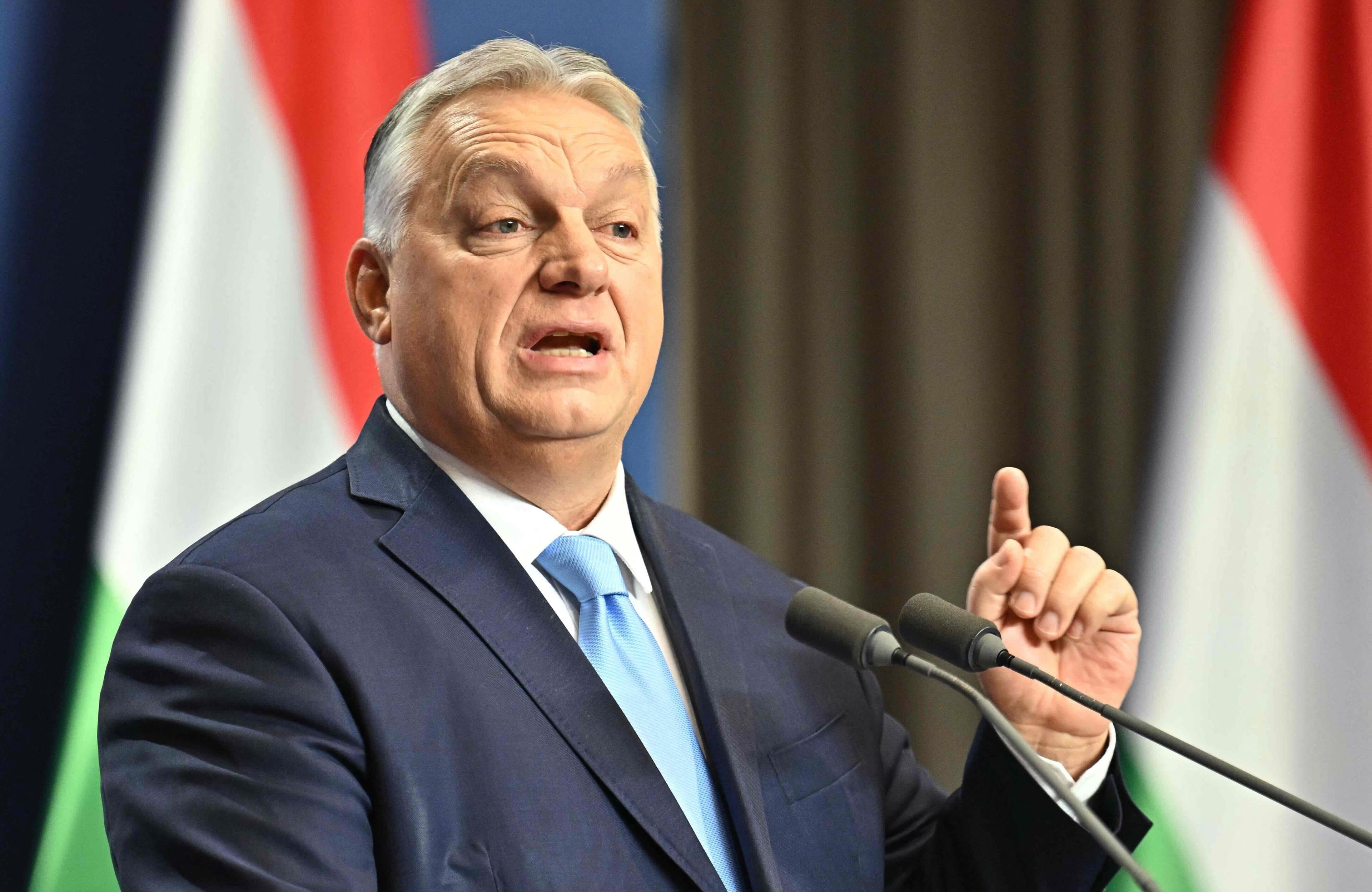 Premier Węgier stoi przed mikrofonem na tle węgierskich flag