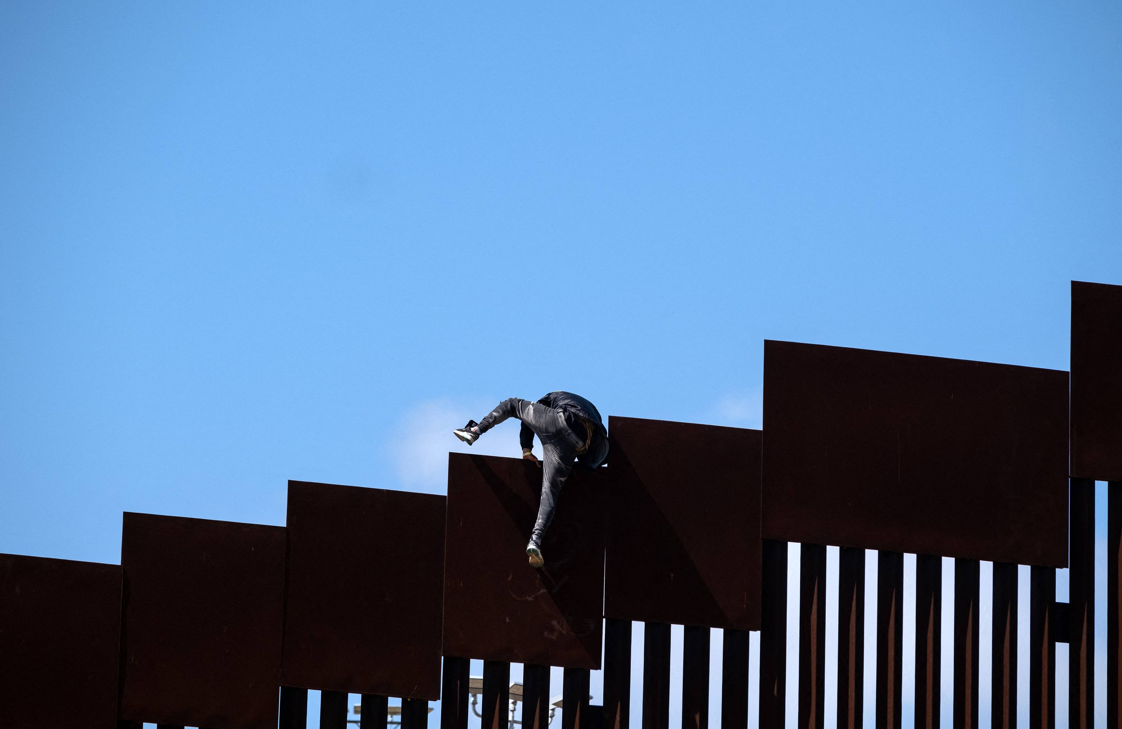 Migrant wspina się przez ogrodzenie graniczne do Stanów Zjednoczonych
