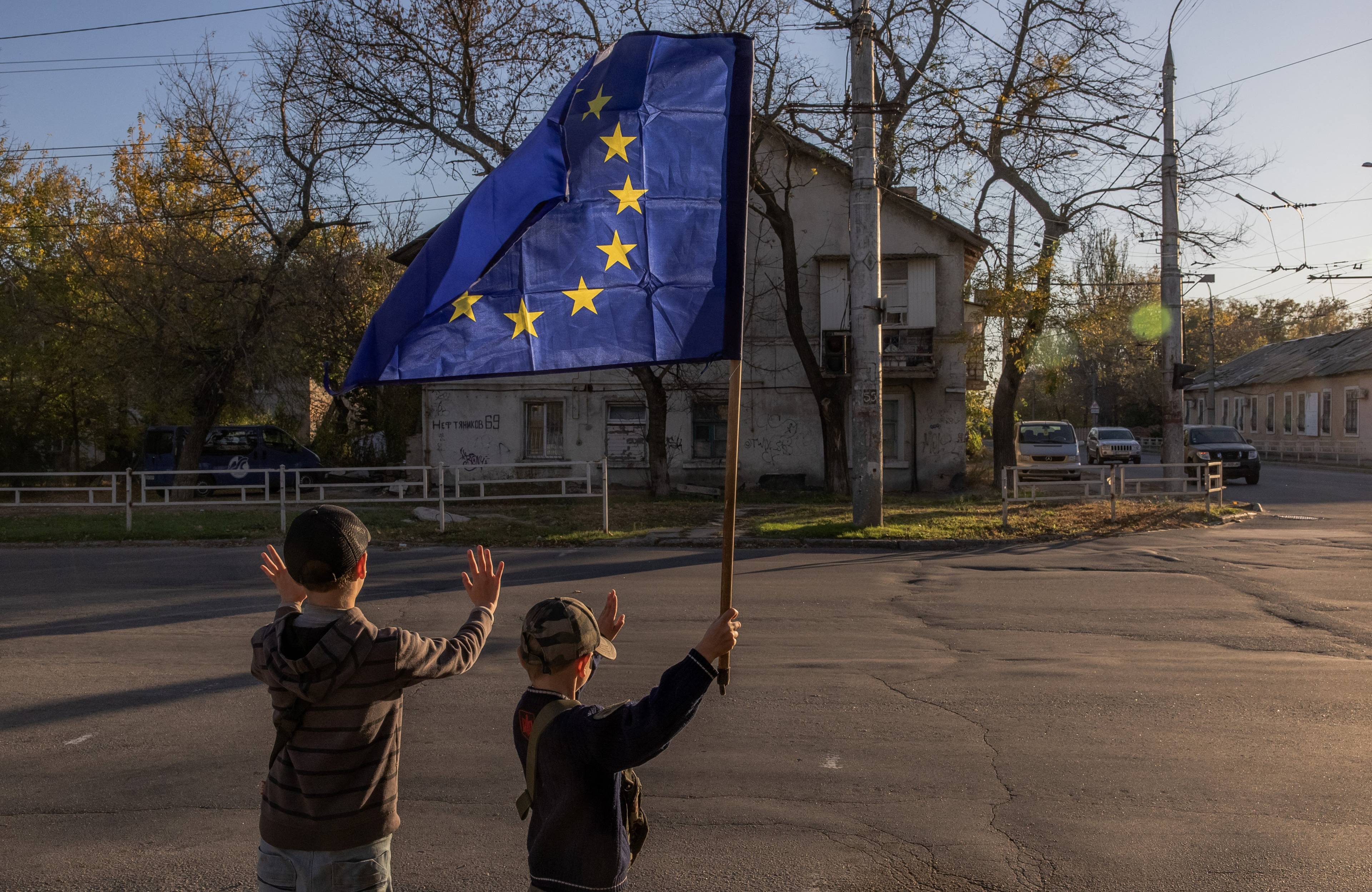 Dwóch chłopców na drodze. Jeden z nich trzyma flagę Unii Europejskiej.