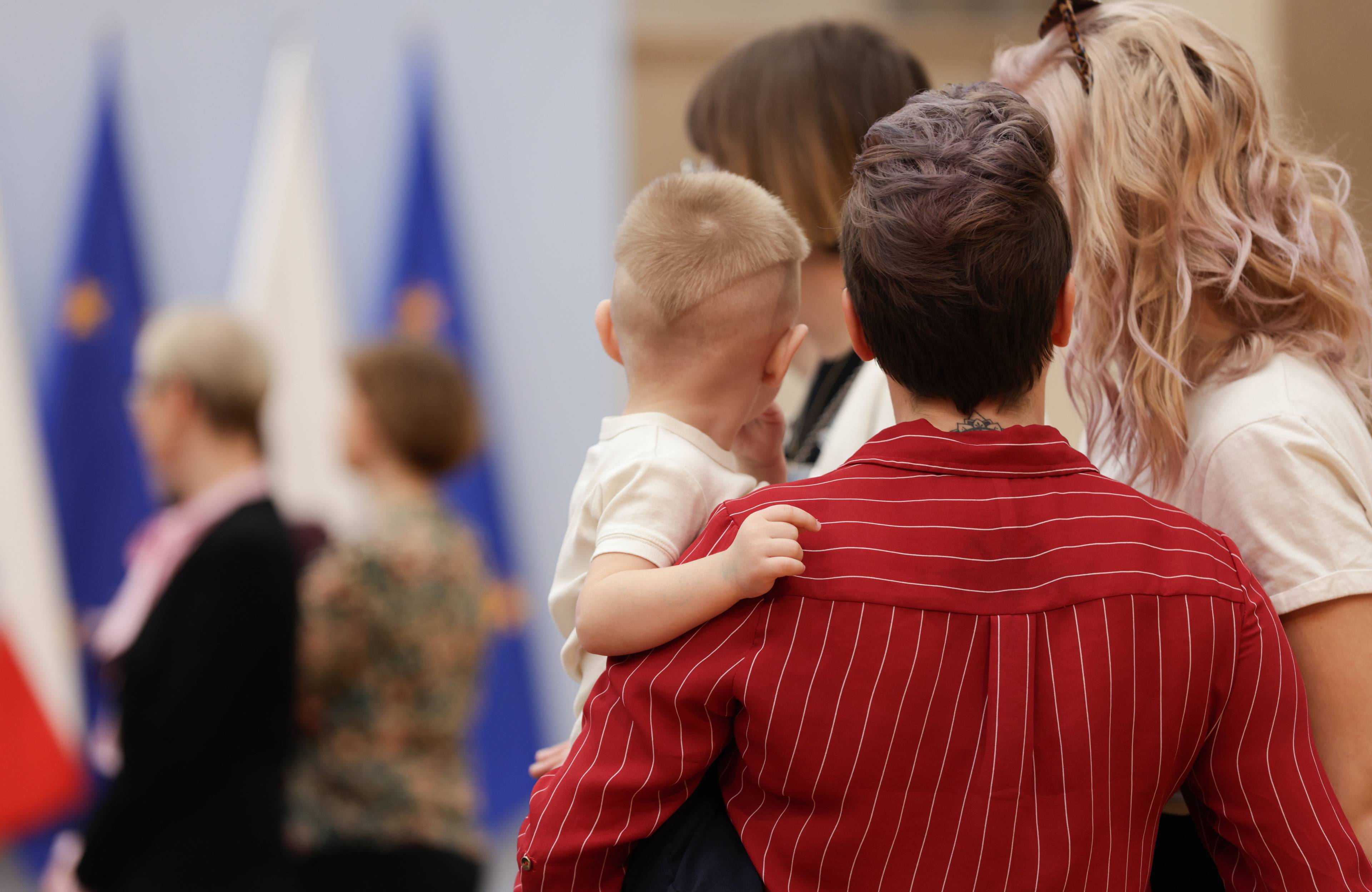 Ludzie z dziećmi na rękach, w tle - polska i unijna flaga