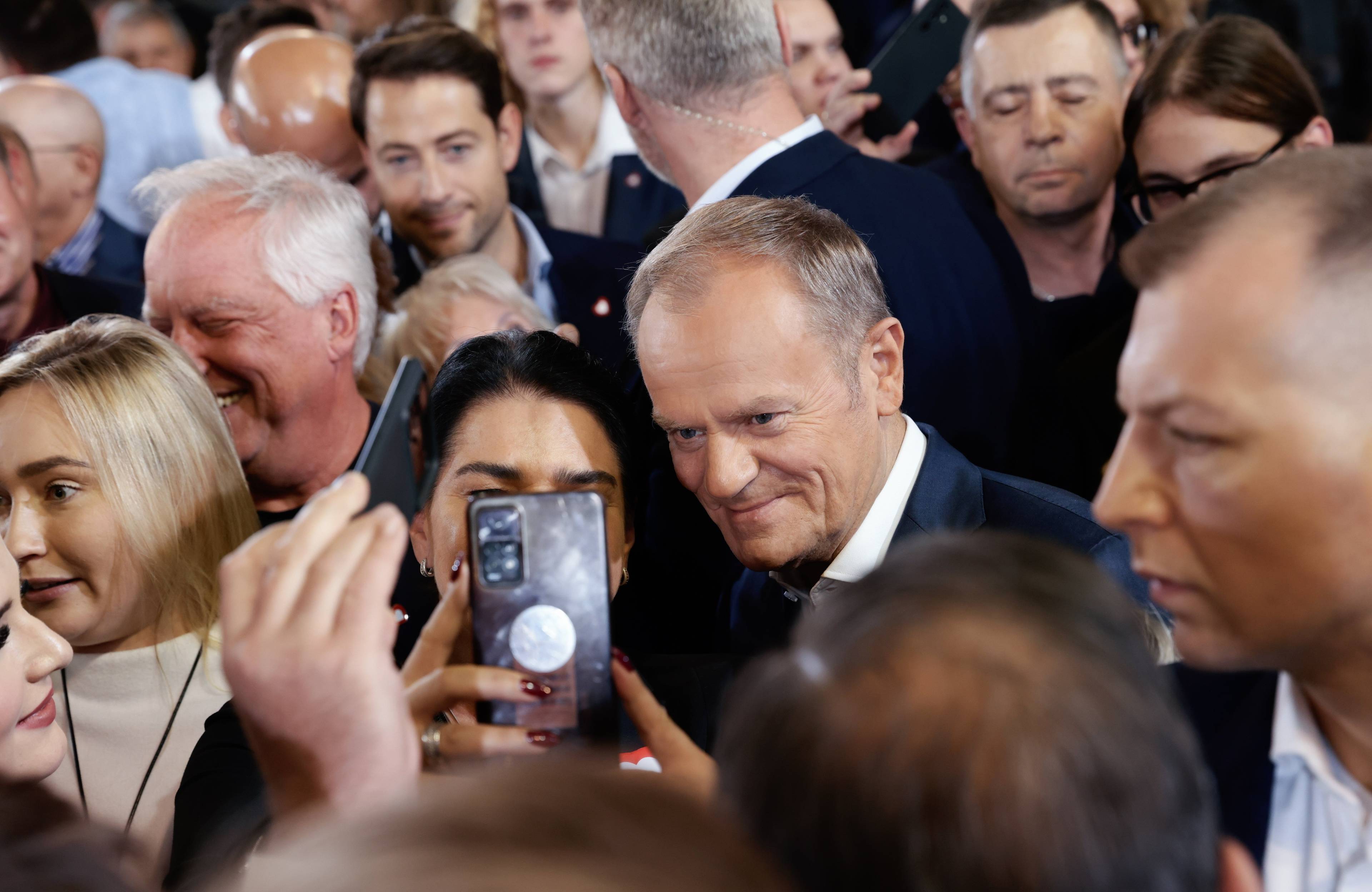 Donald Tusk w otoczeniu zwolenników robi sobie z nimi selfie komórką