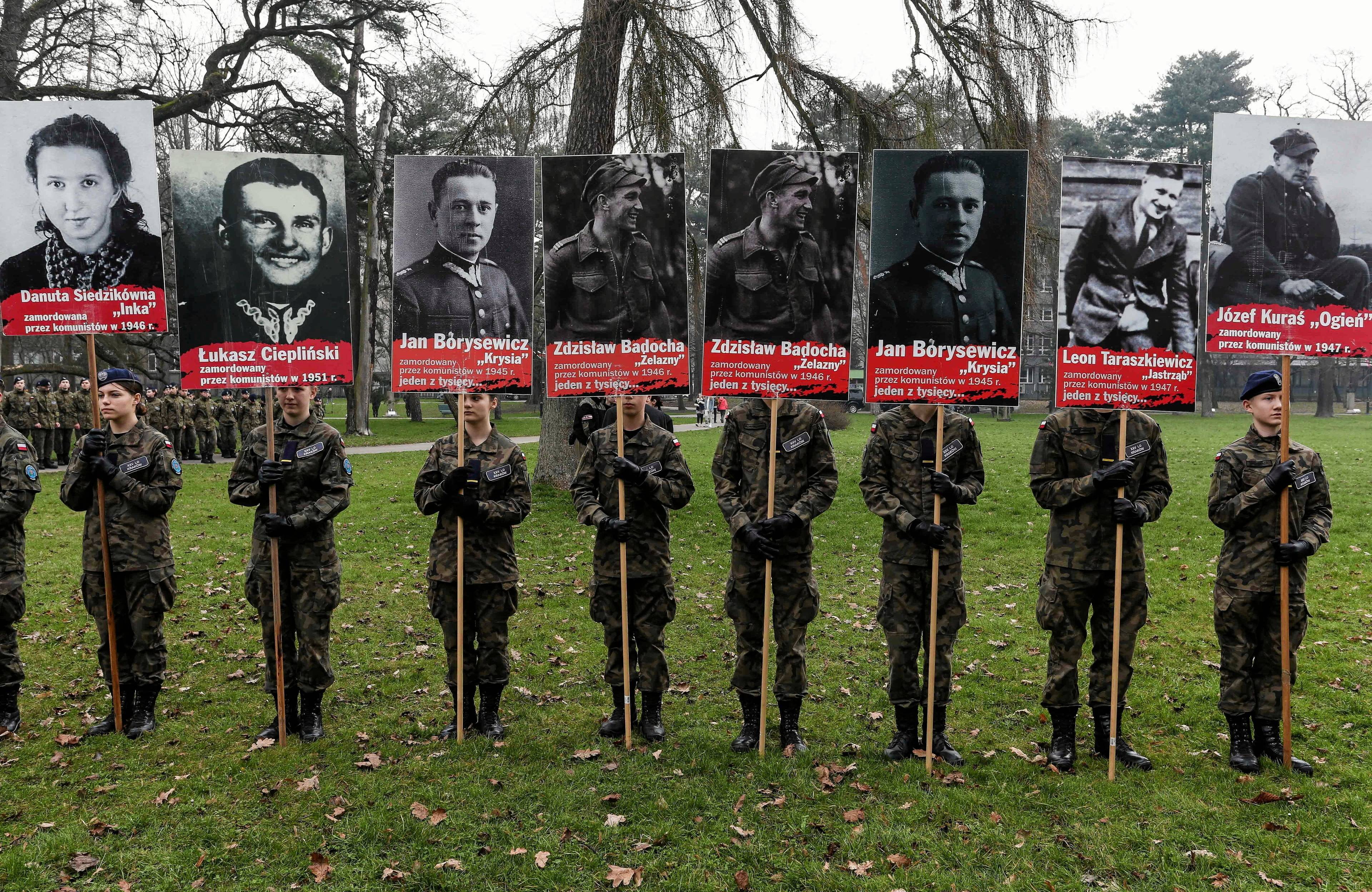 Ośmioro żołnierzy trzyma na drzewcach osiem czarnobiałych portretów