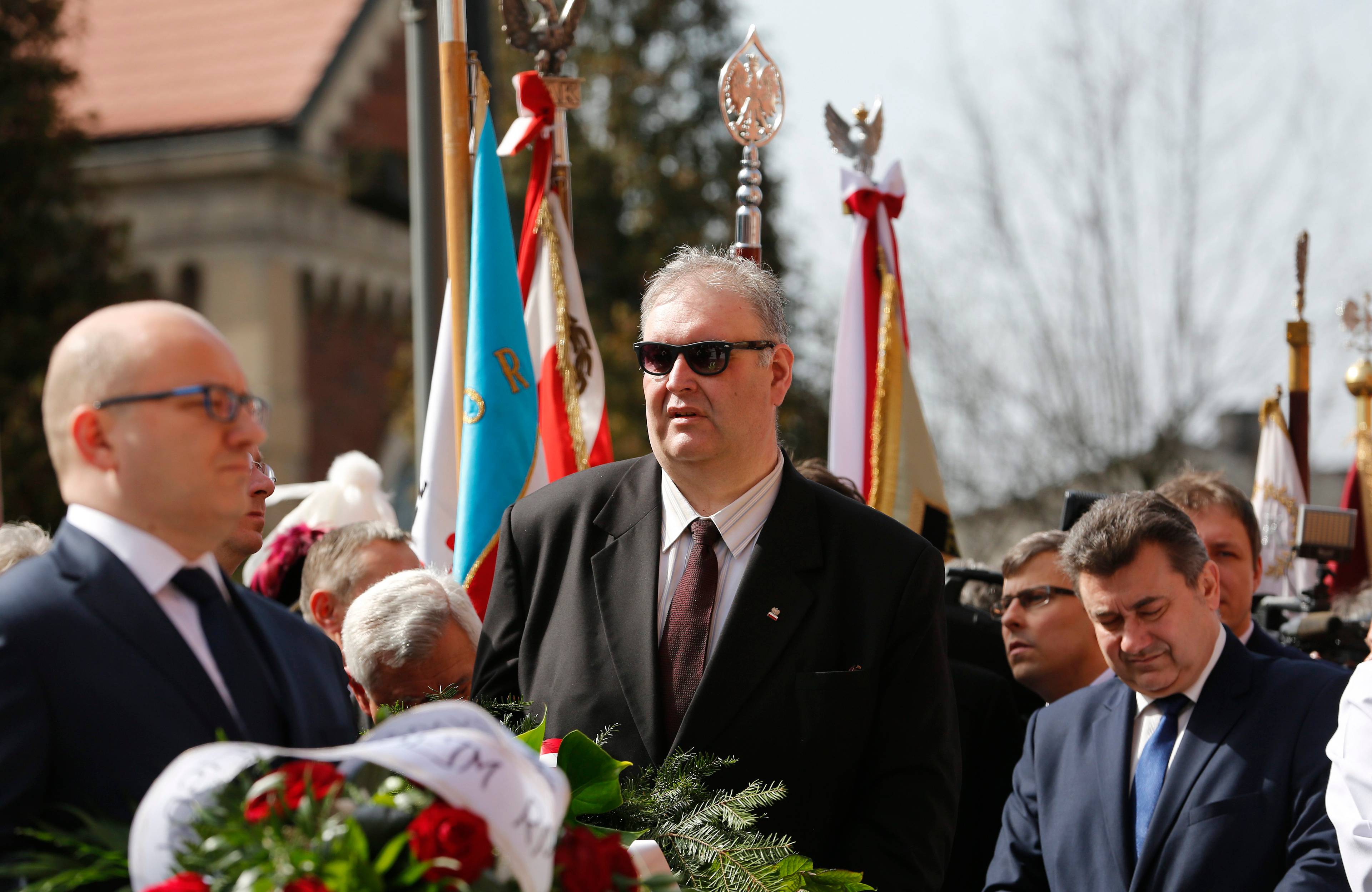 Wysoki mężczyzna w ciemnych okularach na tle sztandarów
