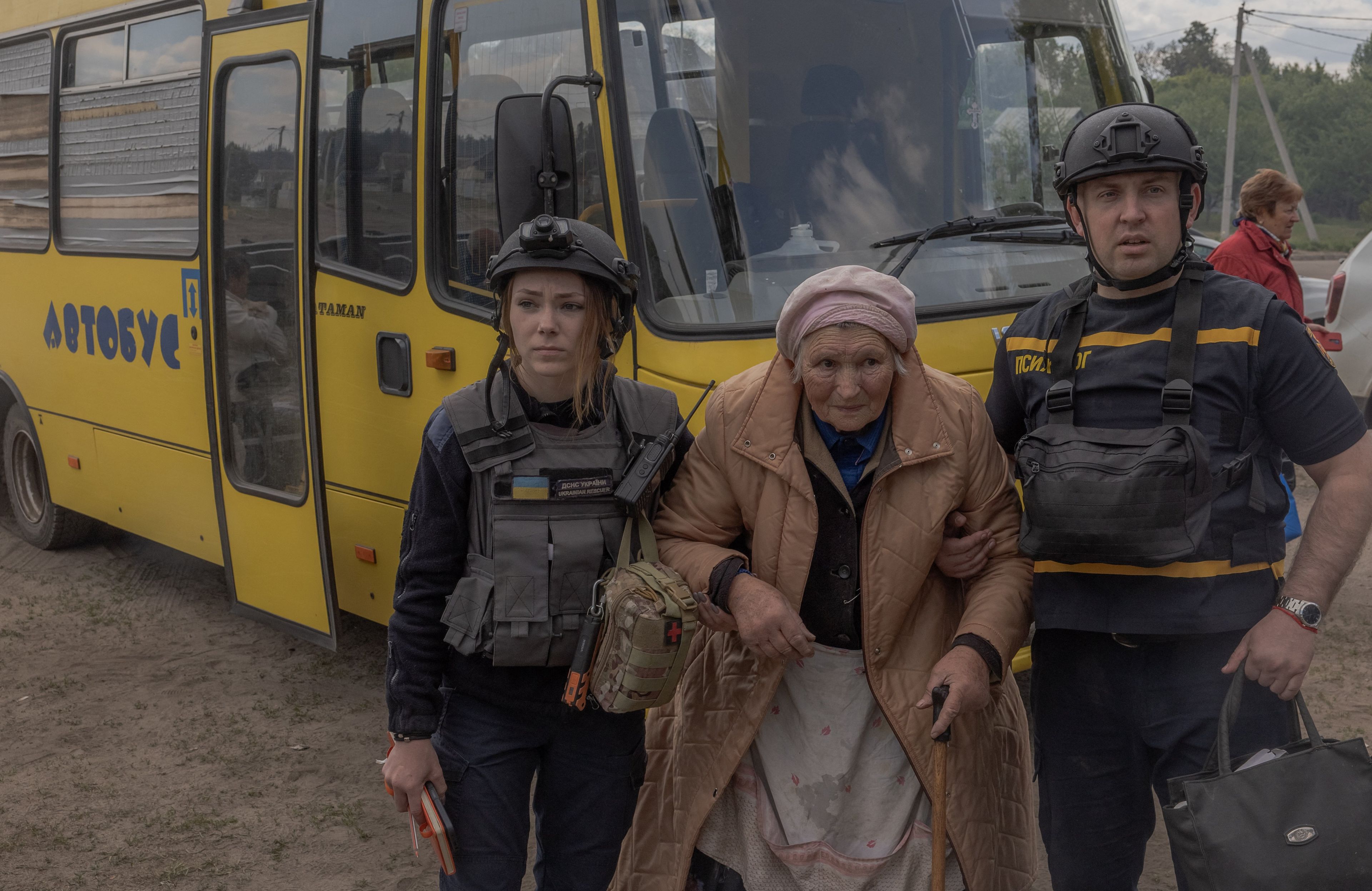 Na zdjęciu są trzy osoby: młoda kobieta, starsza pani i mężczyzna. Stoją obok żółtego autobusu.