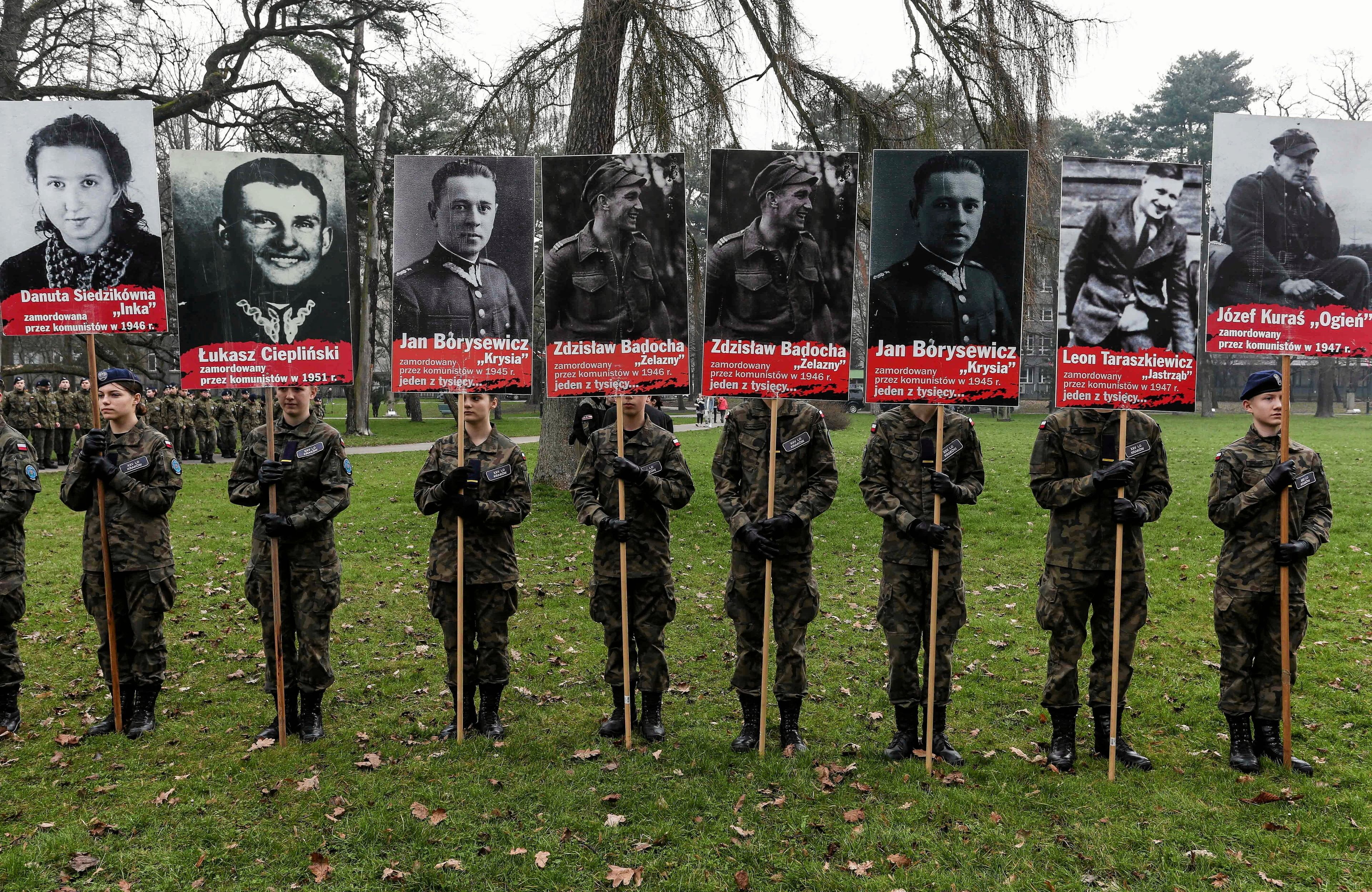 Ośmioro żołnierzy trzyma na drzewcach osiem czarnobiałych portretów