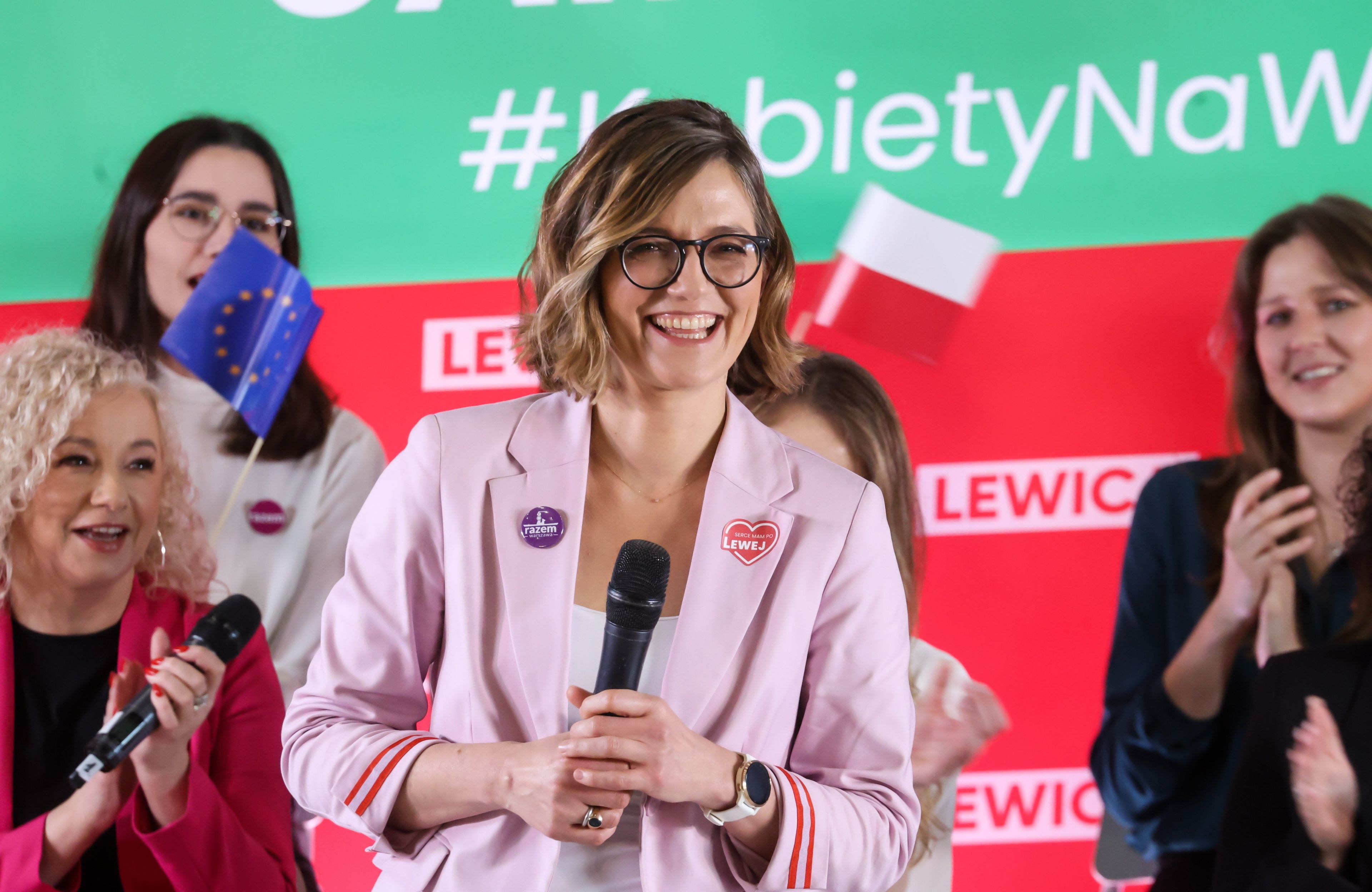 Uśmiechnięta kobieta na tle baneru Lewicy