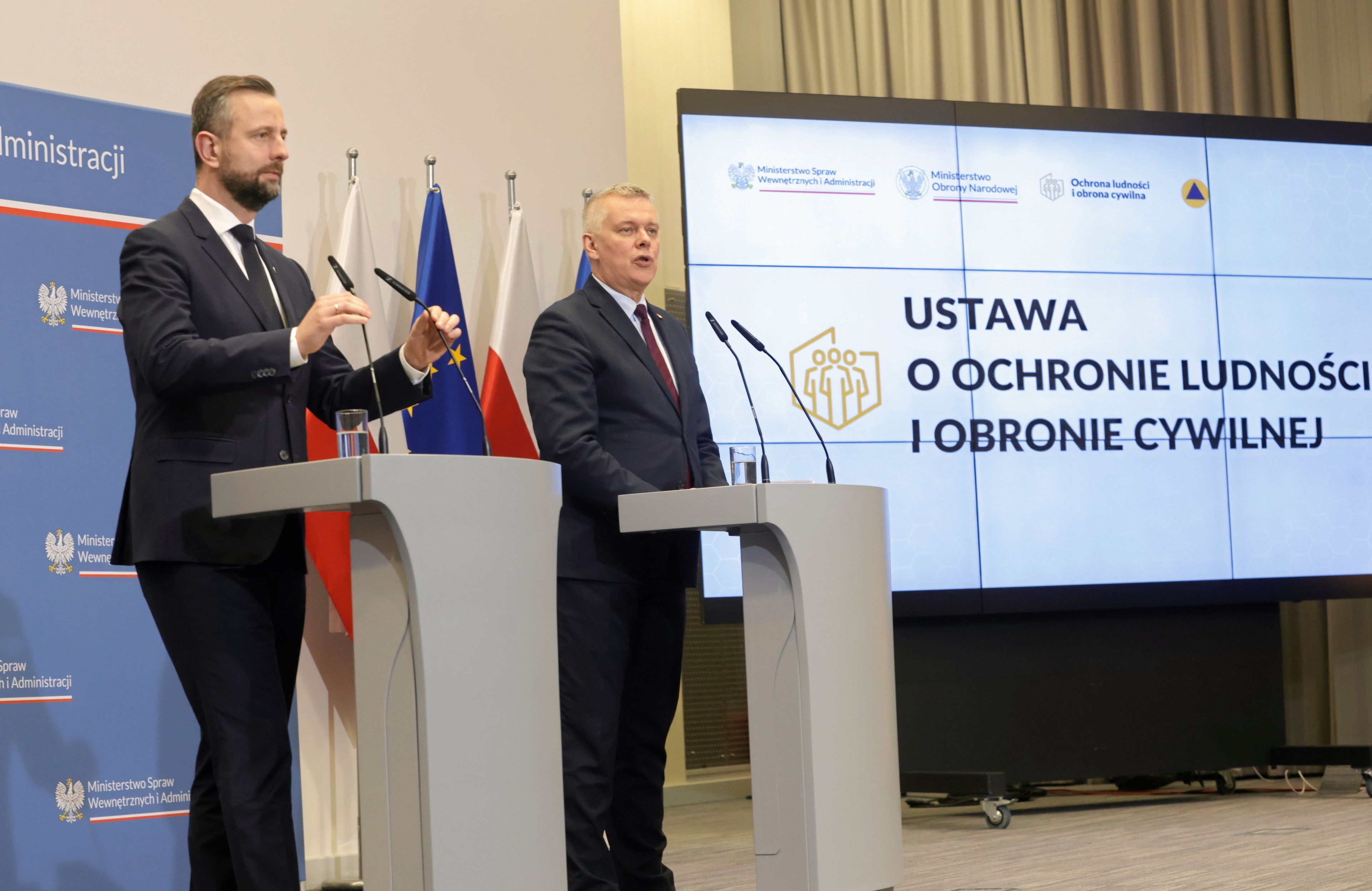 17.12.2024, Warszawa. Szef MON Władysław Kosiniak - Kamysz oraz szef MSWiA i minister koordynator służb specjalnych Tomasz Siemoniak podczas konferencji prasowej dotyczącej ustawy o ochronie ludności i obronie cywilnej. Na zdjęciu dwóch mężczyzn w garniturach stoi przy szarych pulpitach z mikrofonami. Za nimi niebieska ścianka z napisem Ministerstwo Spraw Wewnętrznych i Administracji oraz ekran z napisem "Ustawa o ochronie ludności i obronie cywilnej”
