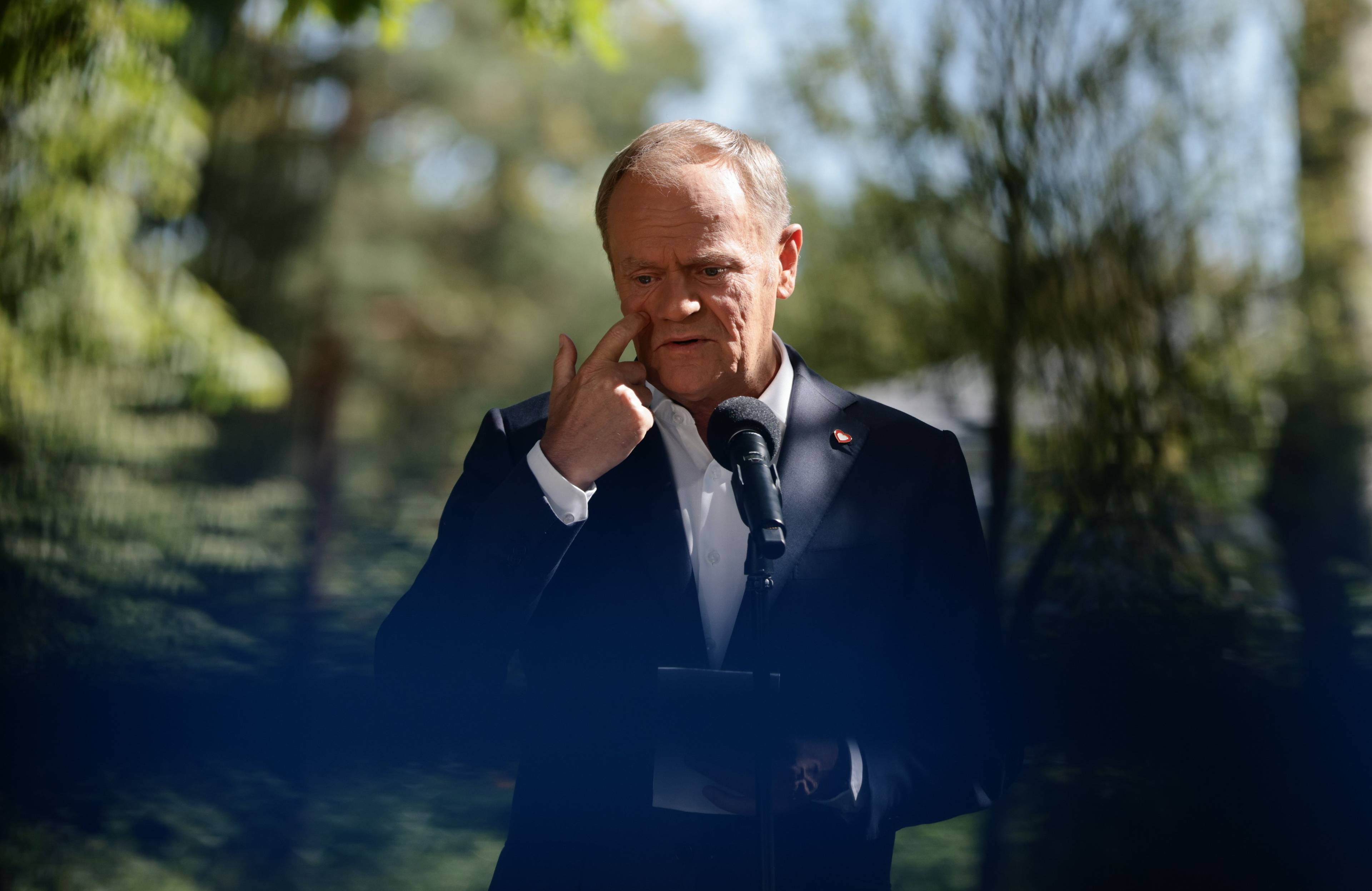 Donald Tusk mówi do mikrofonu na tle drzew