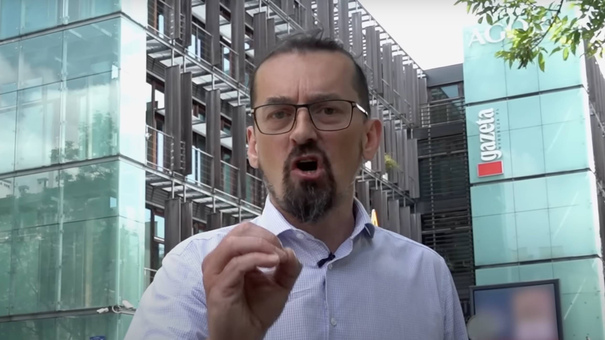 Mariusz Zielke przemawia do kamery na tle budynku Agory z logo "Gazety Wyborczej". Kadr z filmu "Bagno".