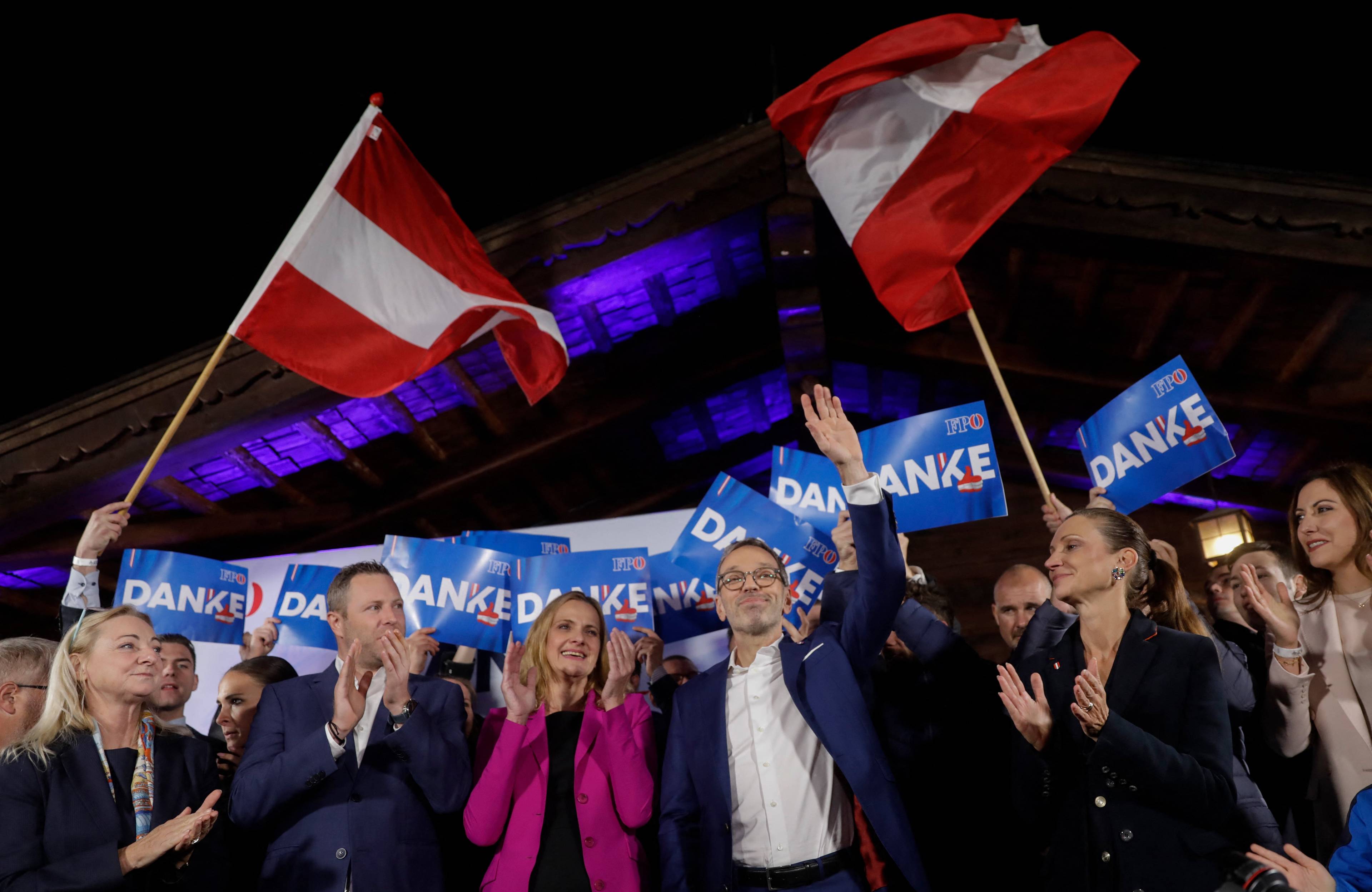 Grupa tryumfujących ludzi pod powiewającymi austriackimi flagami.