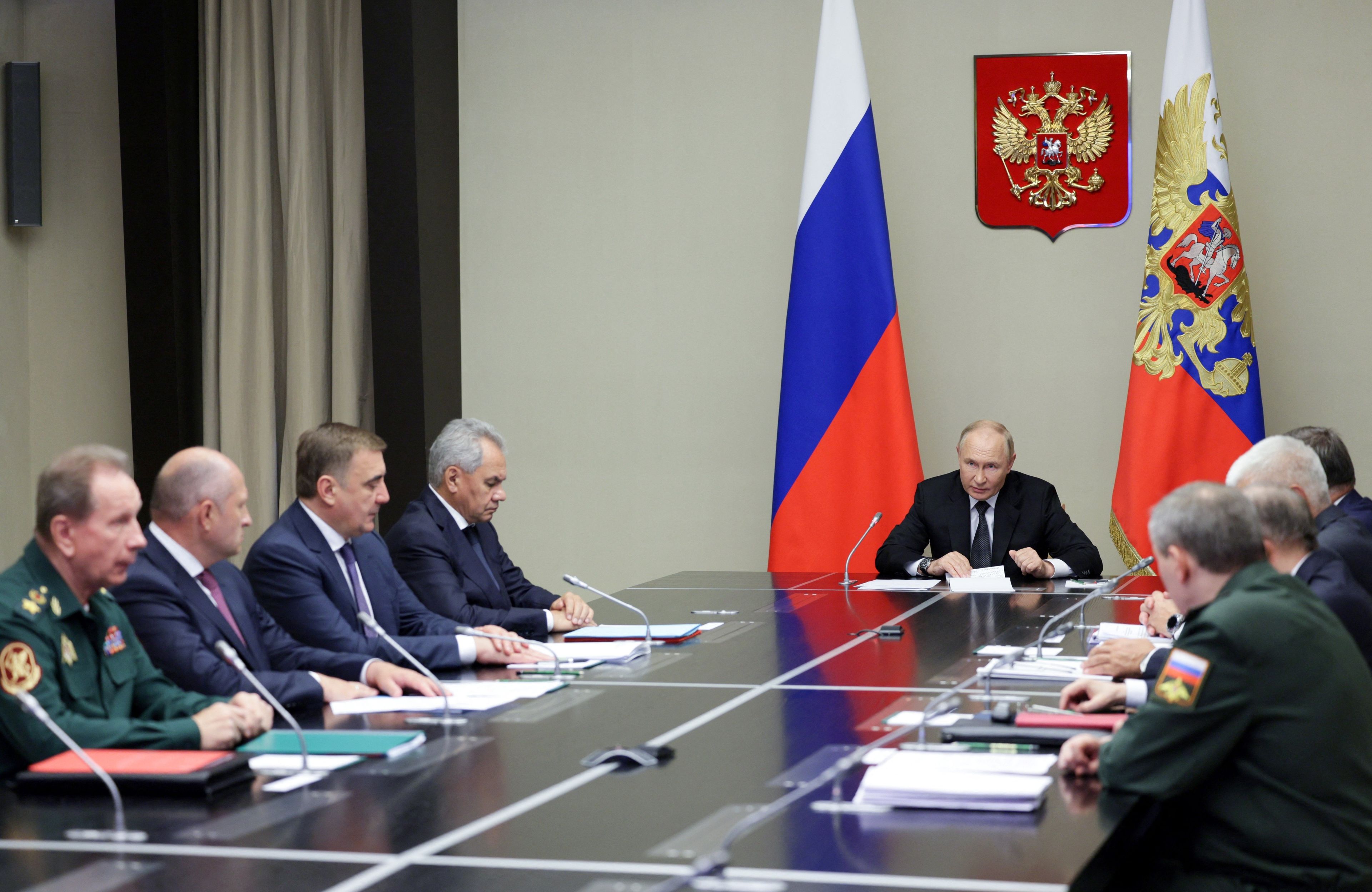 Władimir Putin za stołem wśród oficjeli. W tle flaga Rosji i godło