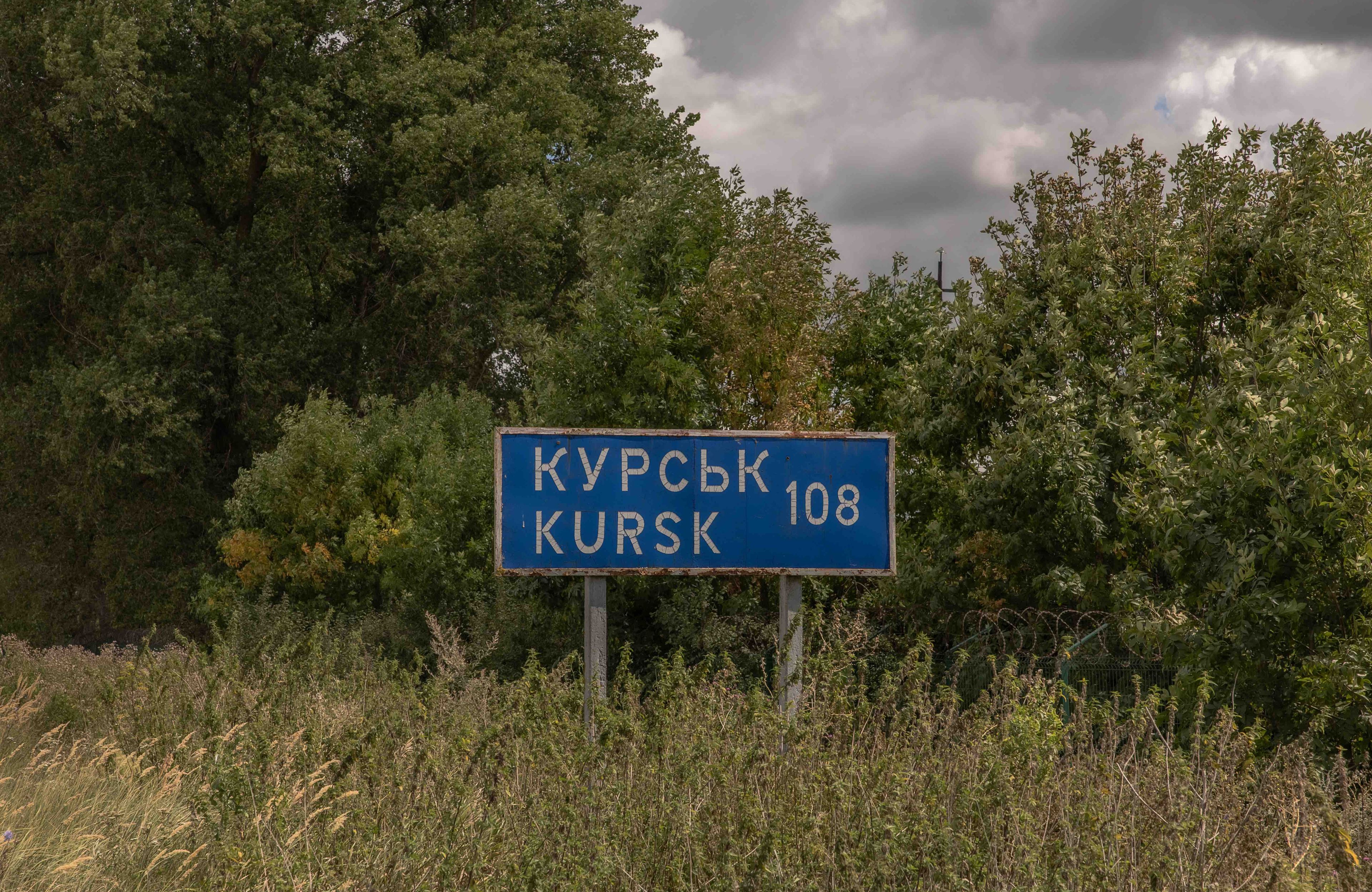 Drogowskaz z napisem Kurs 108 km na skraju drogi, na tle lasu