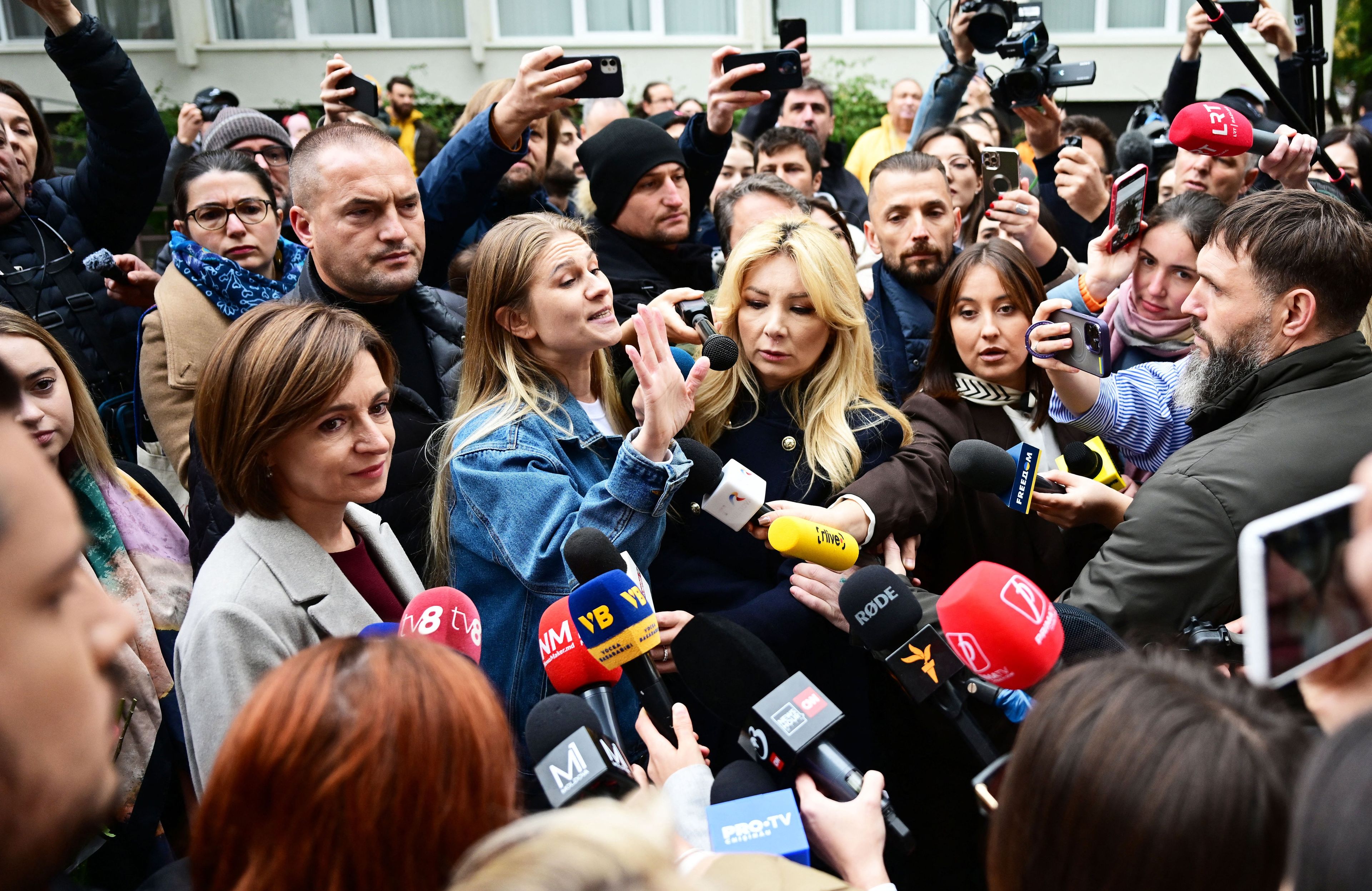 Kobieta w jasnym żakiecie wśród tłumu dziennikarzy