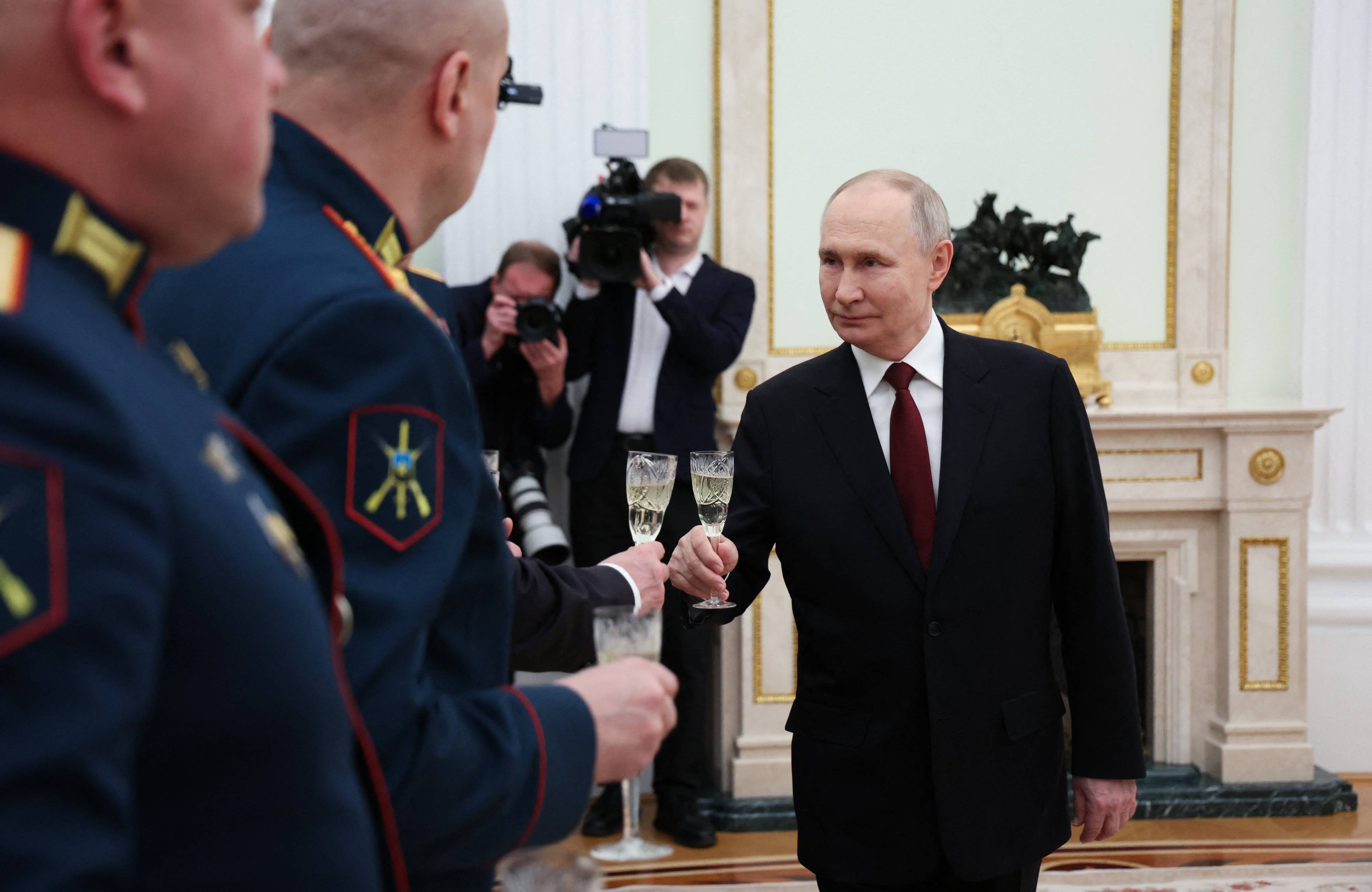 Władimir Putin trzyma w ręku lampka szampana, wokół niego wojskowi