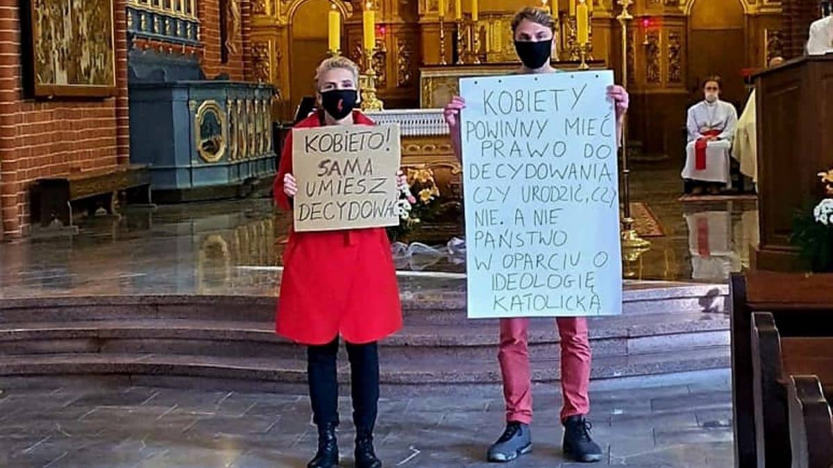 Joann Sceuring-Wielgus z mężem w kościele, stoją w maseczkach w nawie głównej tyłem do ołtarza, w rękach trzymają plakaty o prawach kobiet