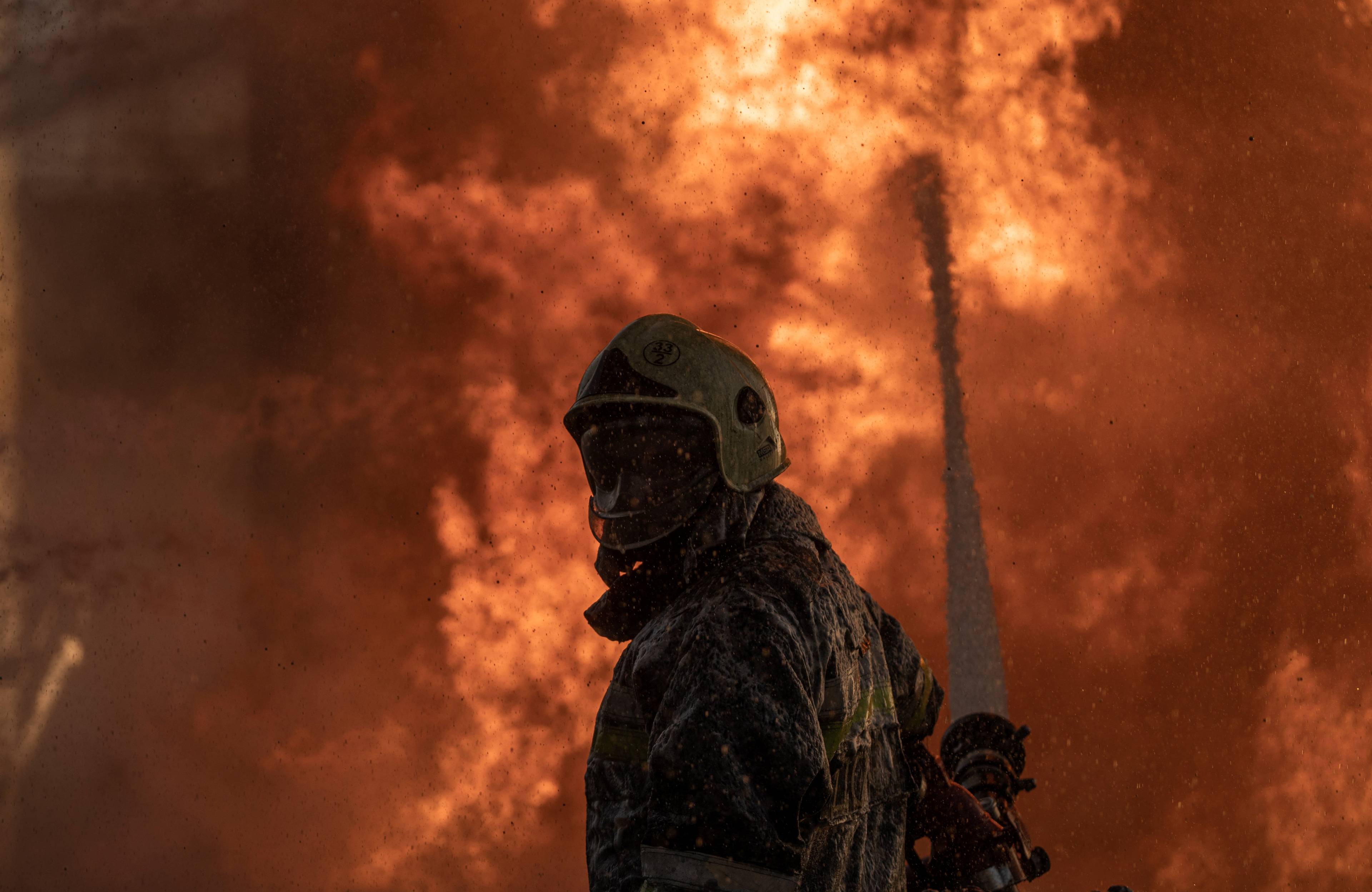 Na zdjęciu widać ukraińskiego strażaka, który stoi wśrodku pomarańczonego ognia. Mężczyzna gasi pożar spowodowany rosyjskim atakiem 12 czerwca 2024 roku